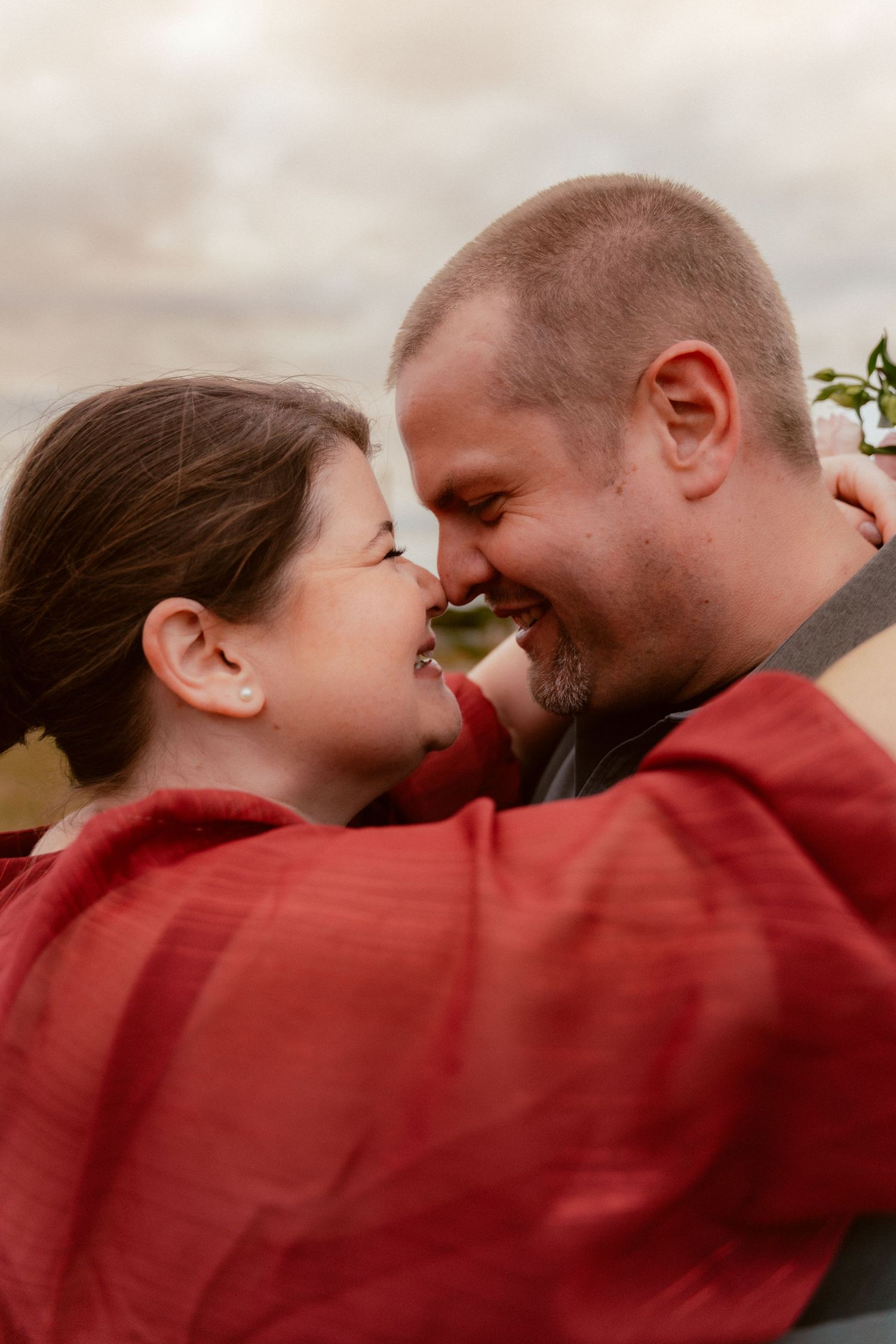 A romantic close-up of a couple touching noses and smiling while wearing red clothing.