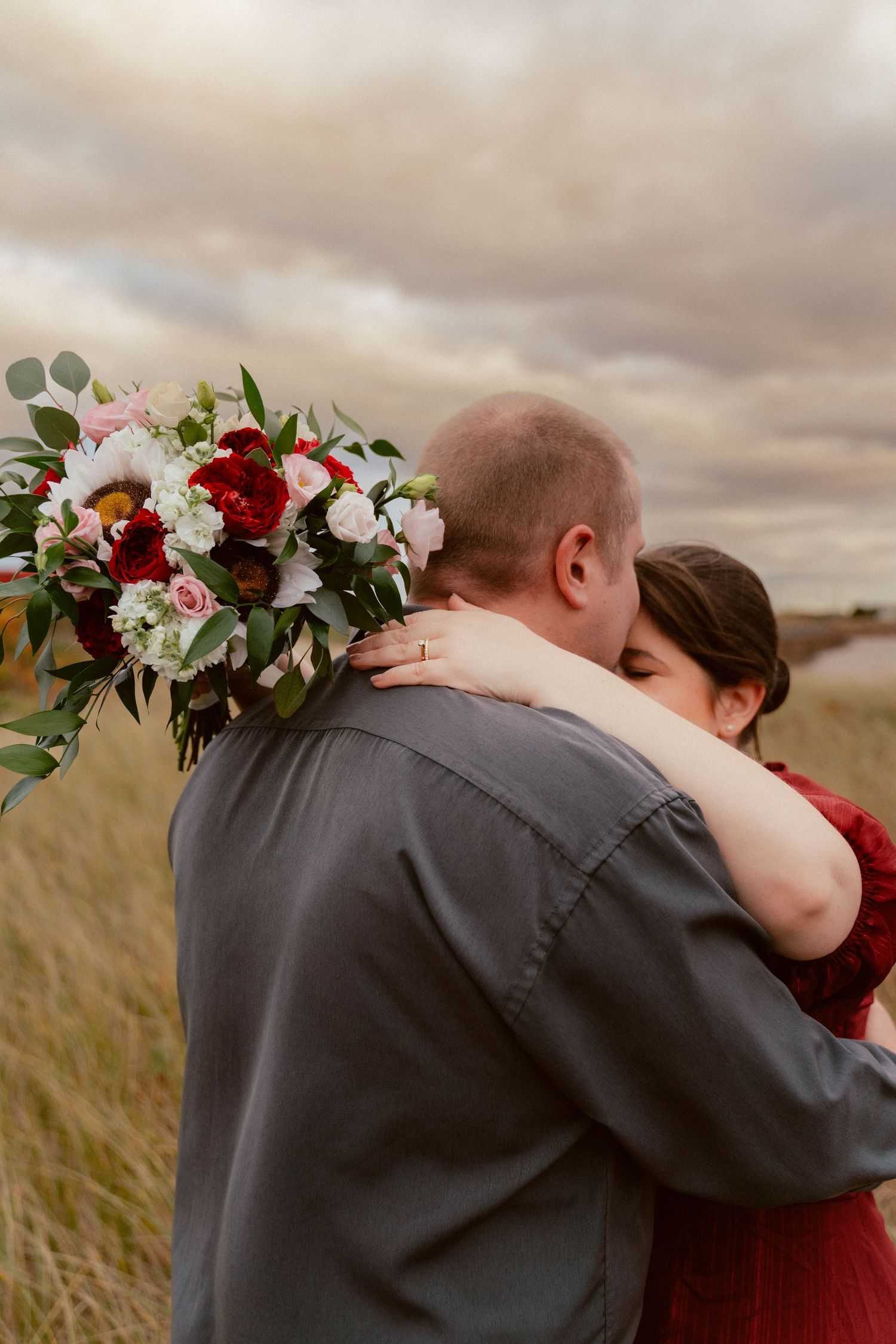 An intimate embrace captured outdoors with a beautiful floral bouquet in view.
