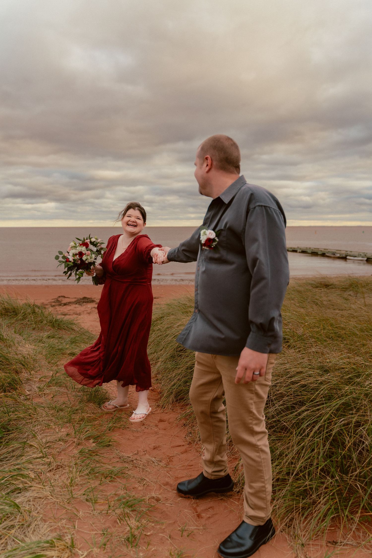 A couple laughs together on a coastal cliff during their wedding photoshoot.