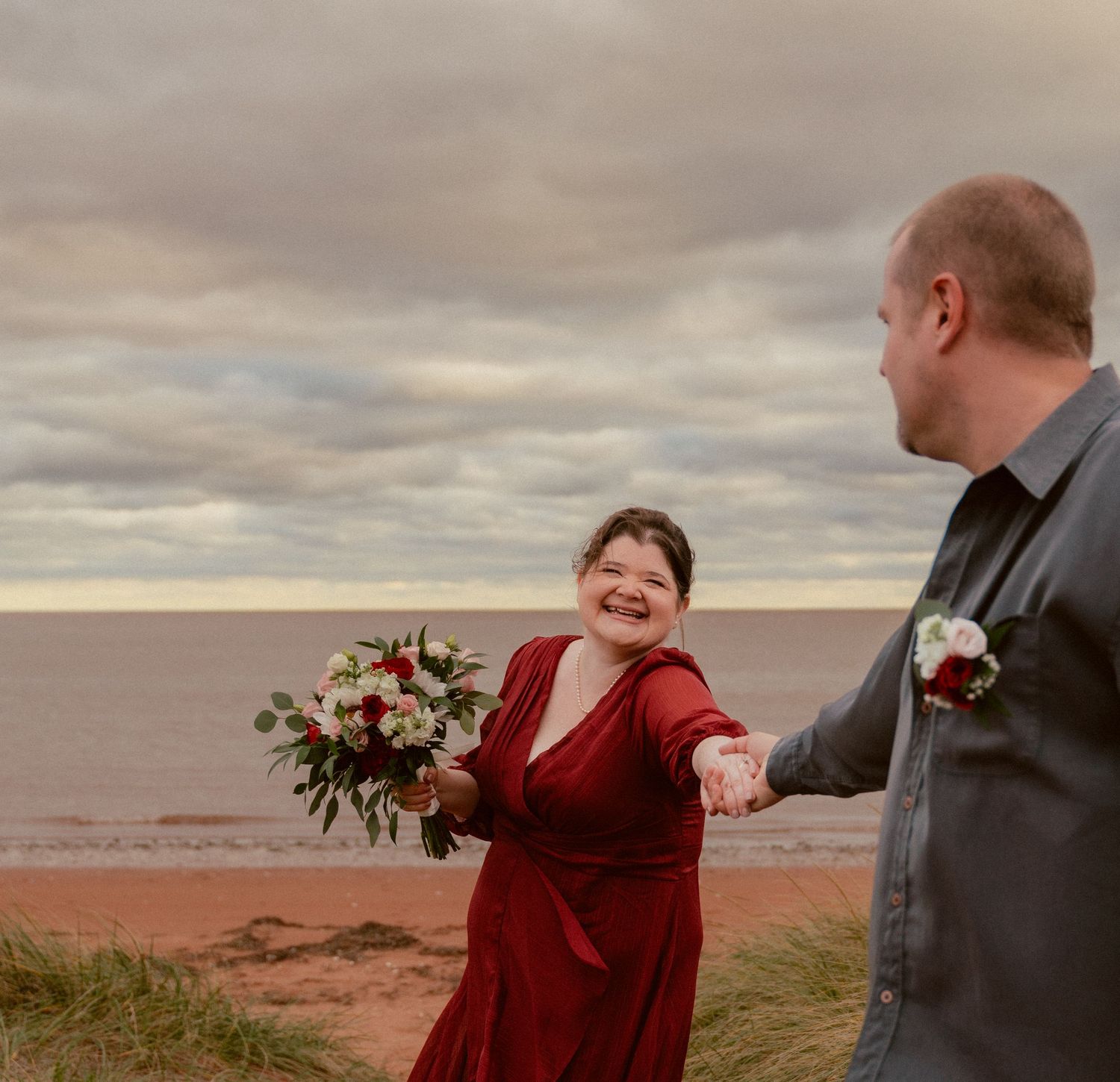 A couple shares a playful moment on a coastal cliff with dramatic cloudy skies.