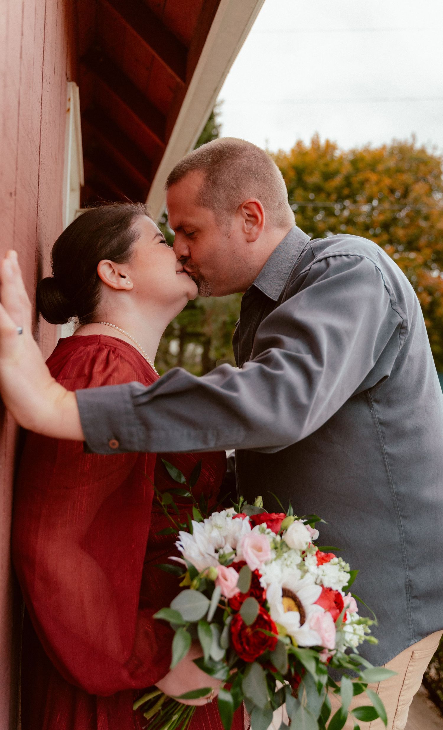 A tender moment shared near a red barn wall with a beautiful mixed flower bouquet.