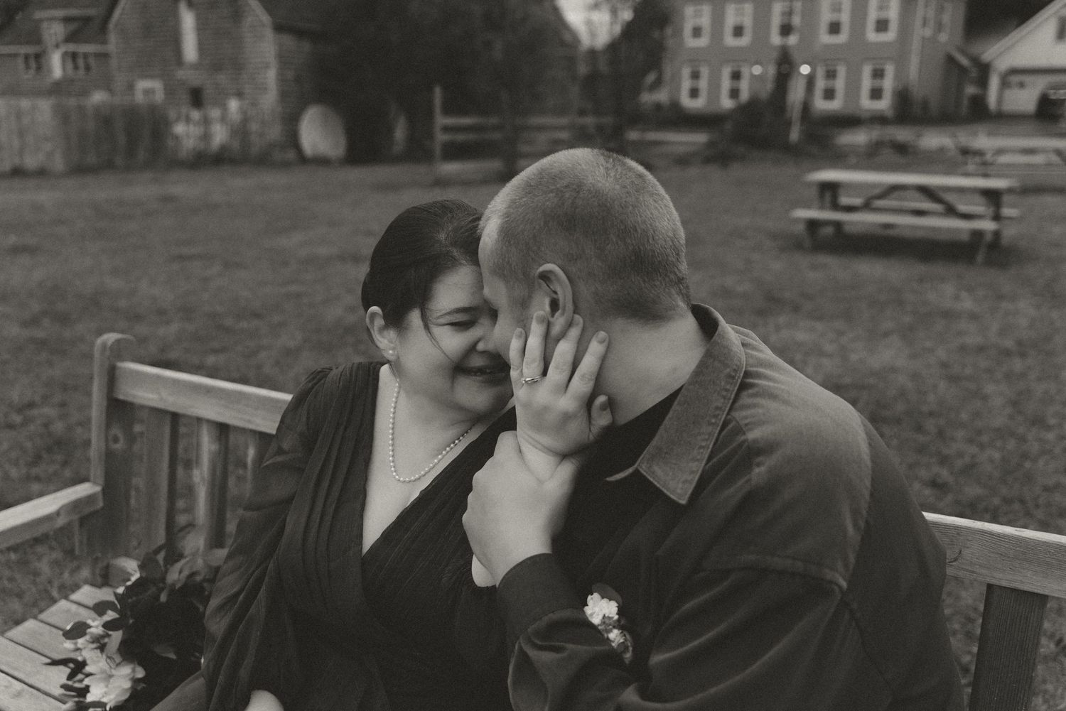 An intimate black and white portrait of a couple sharing a tender moment on a bench.