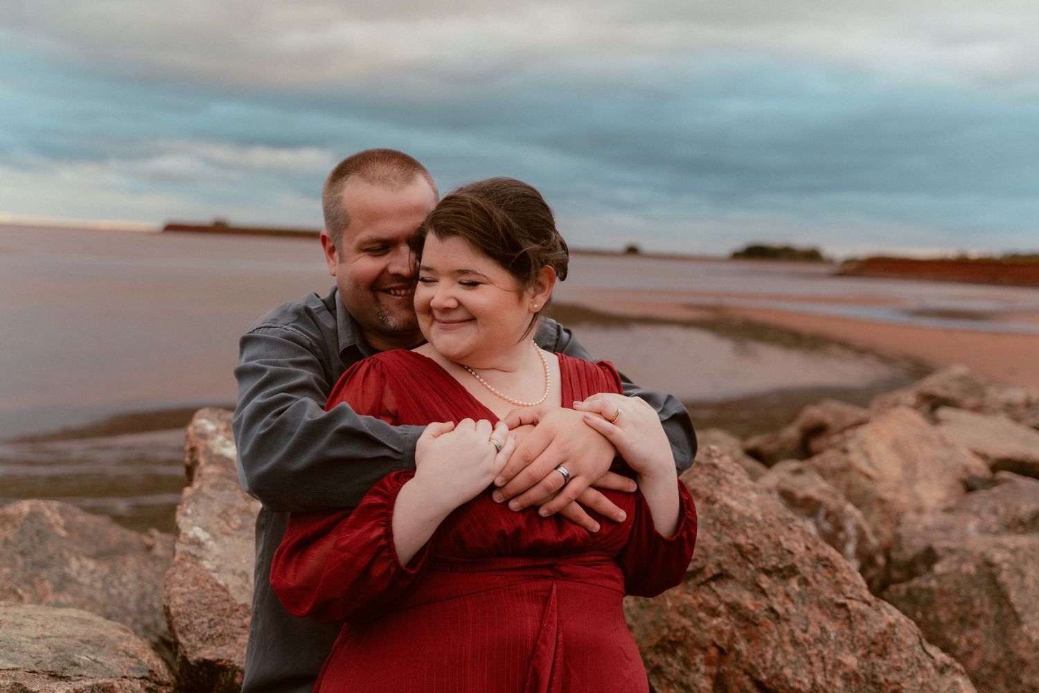 A loving embrace on coastal rocks during sunset with ocean waves in background.