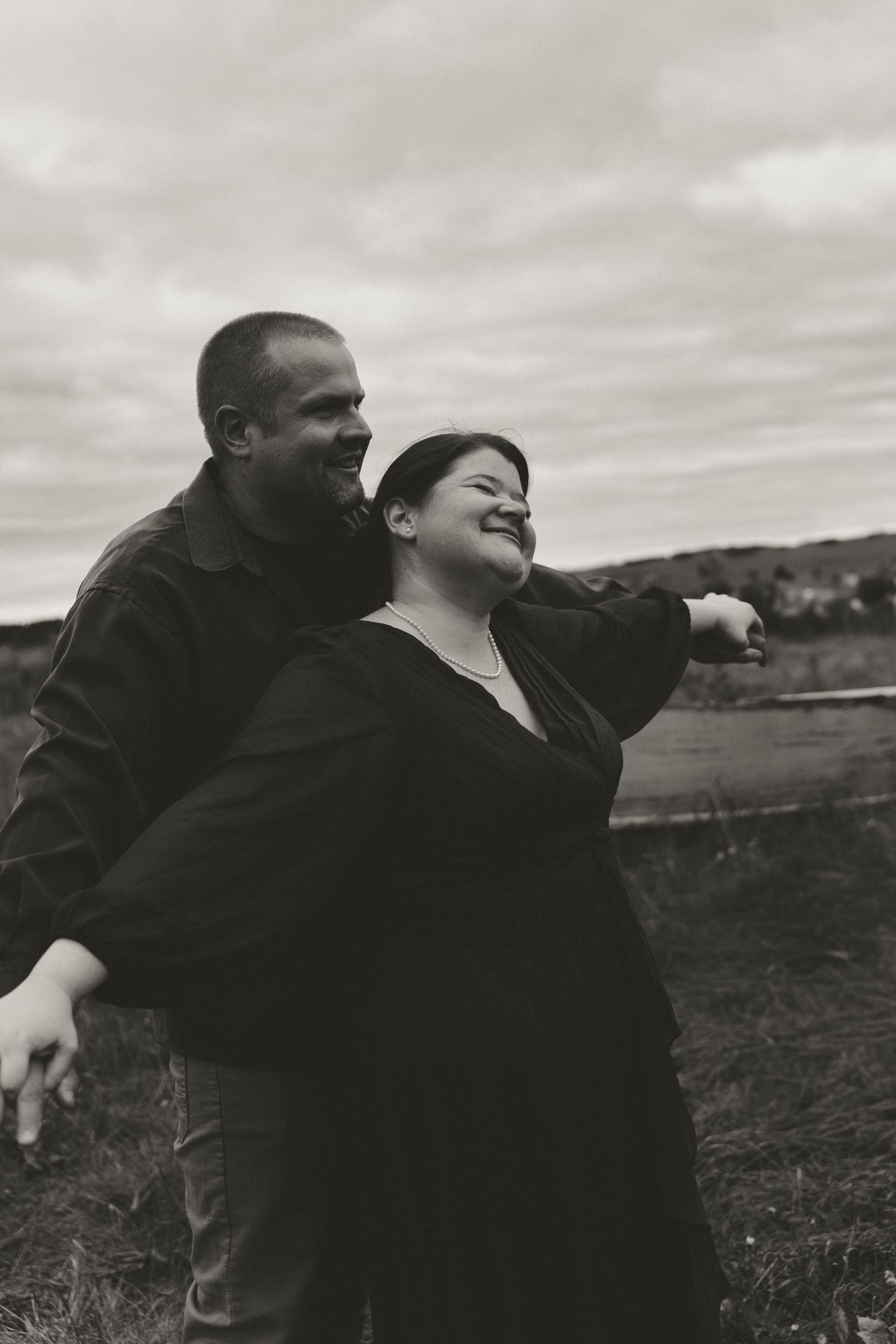 A candid black and white photo of a couple sharing laughter in an outdoor setting.