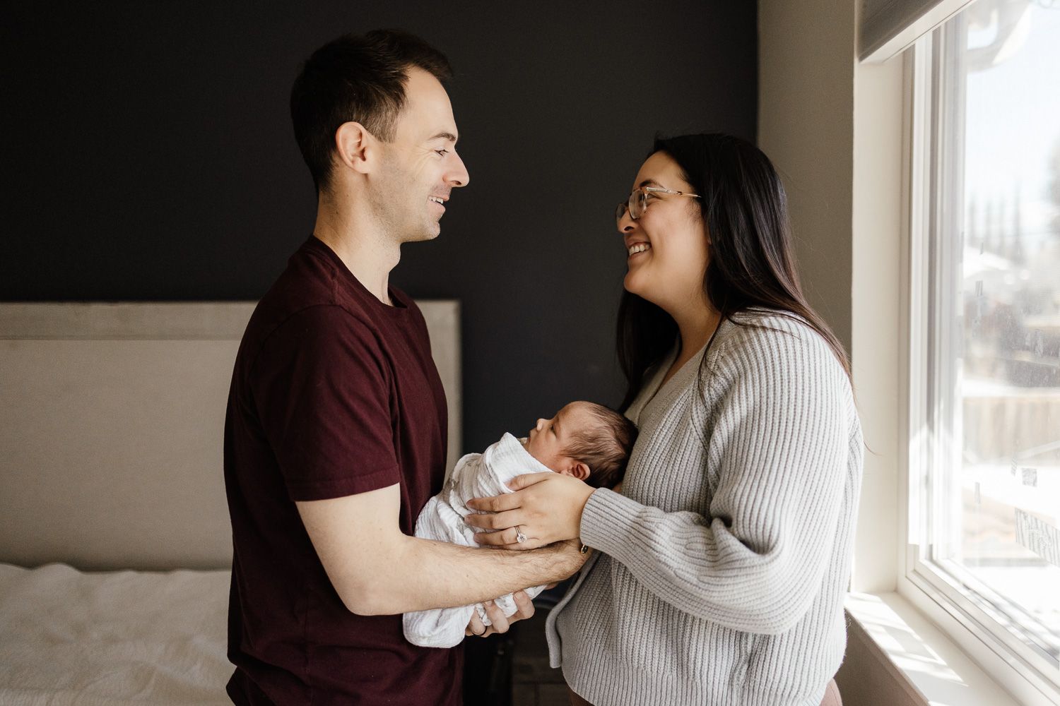 Mom and dad smile at each other while holding their baby between them at their San Jose in-home newborn photo session