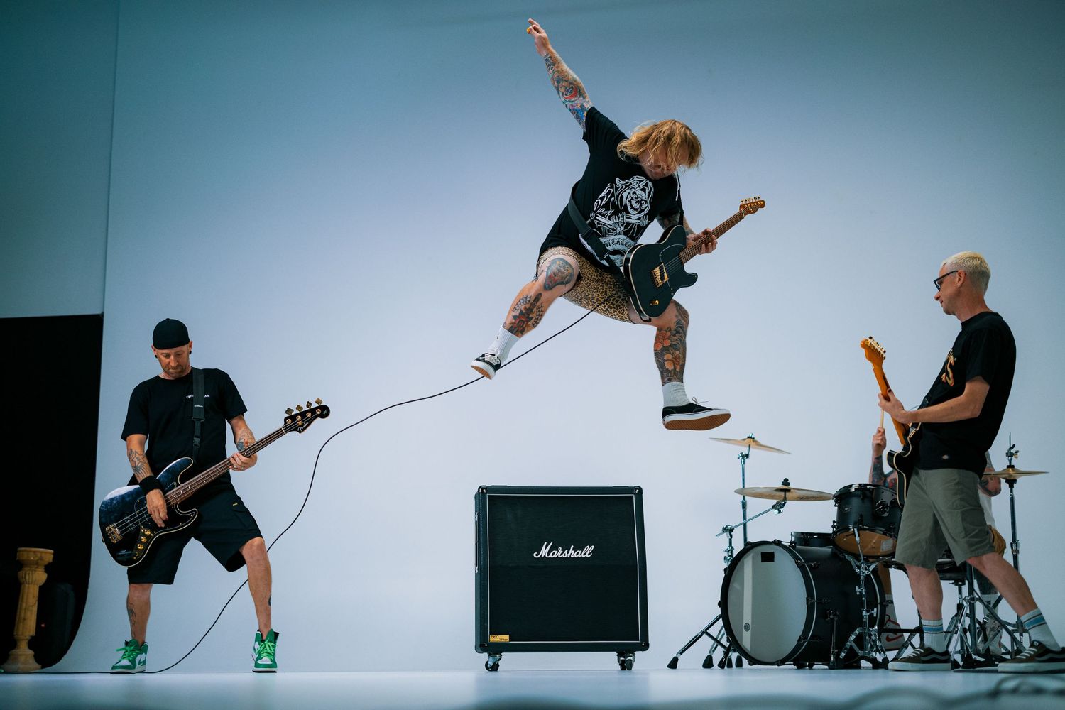 Musician jumps mid-air between bandmates while performing with guitar and Marshall amp on stage.