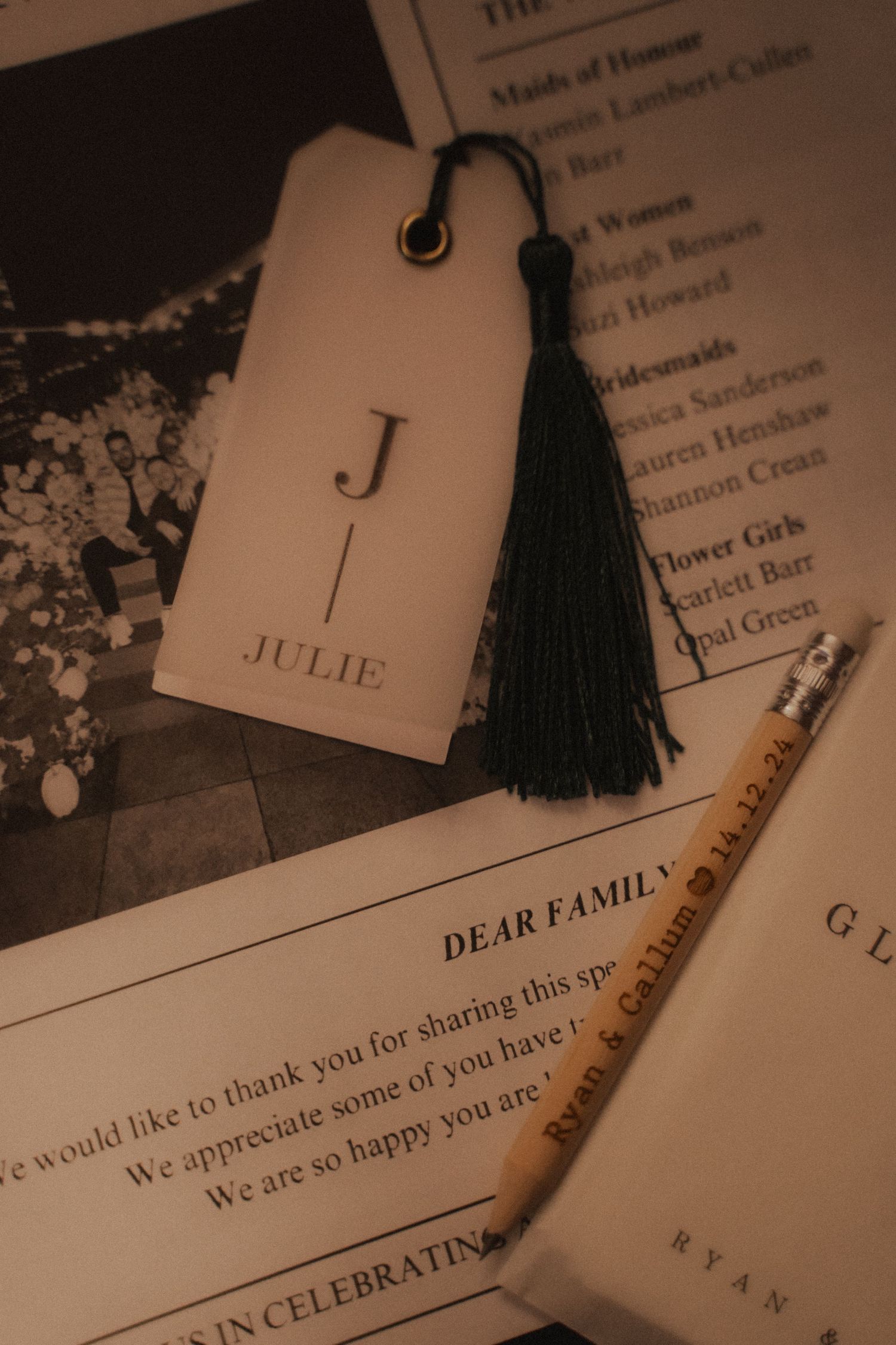 A sepia-toned photo of a name tag with the letter J and black tassel alongside invitation paper that reads Dear Family.