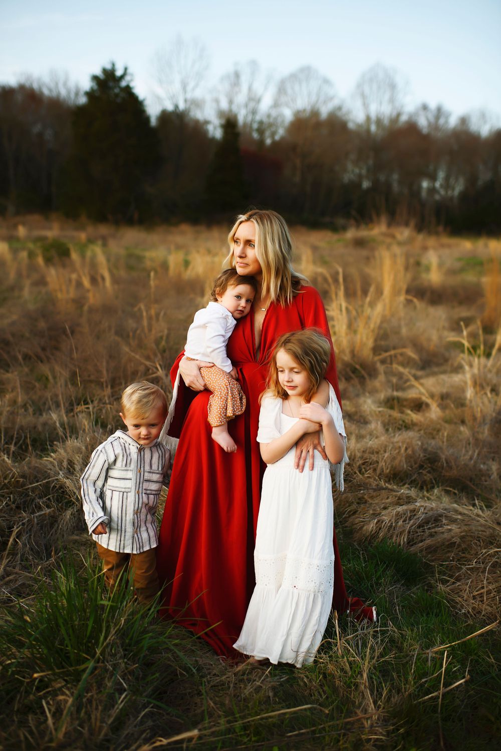 A family in a field at sunset wearing red and white dresses with tall grass and trees in the background.