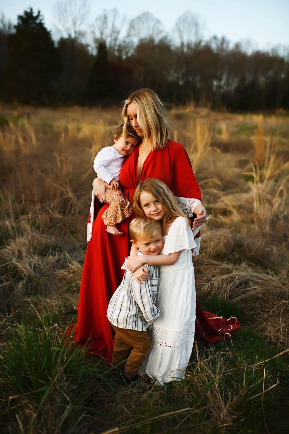 A group in a field at sunset, wearing flowing dresses in red and white amidst tall golden grass.