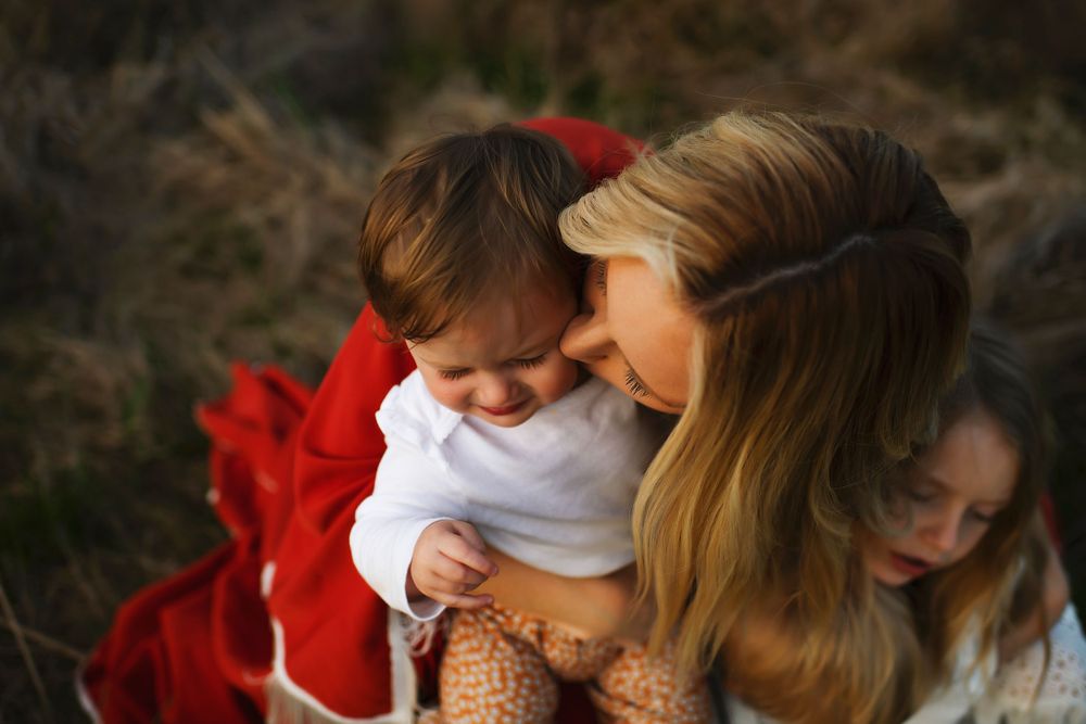 A tender family moment captured outdoors with red blanket and soft afternoon light.