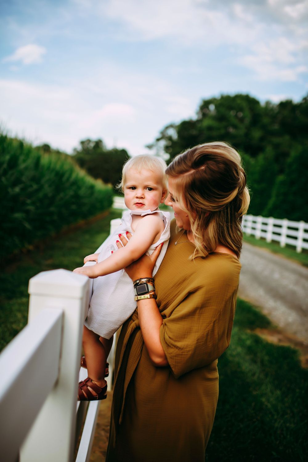 Parent and child spending time together on a white fence-lined country road on a sunny afternoon.