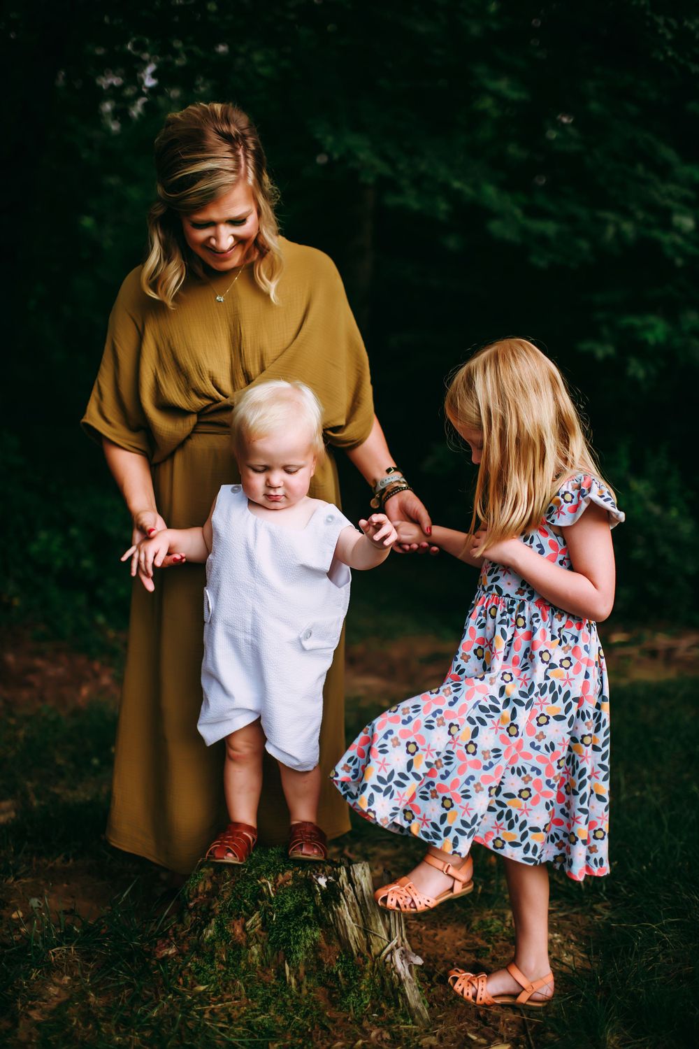 A family shares a tender moment together while standing by a tree stump in a wooded outdoor setting.