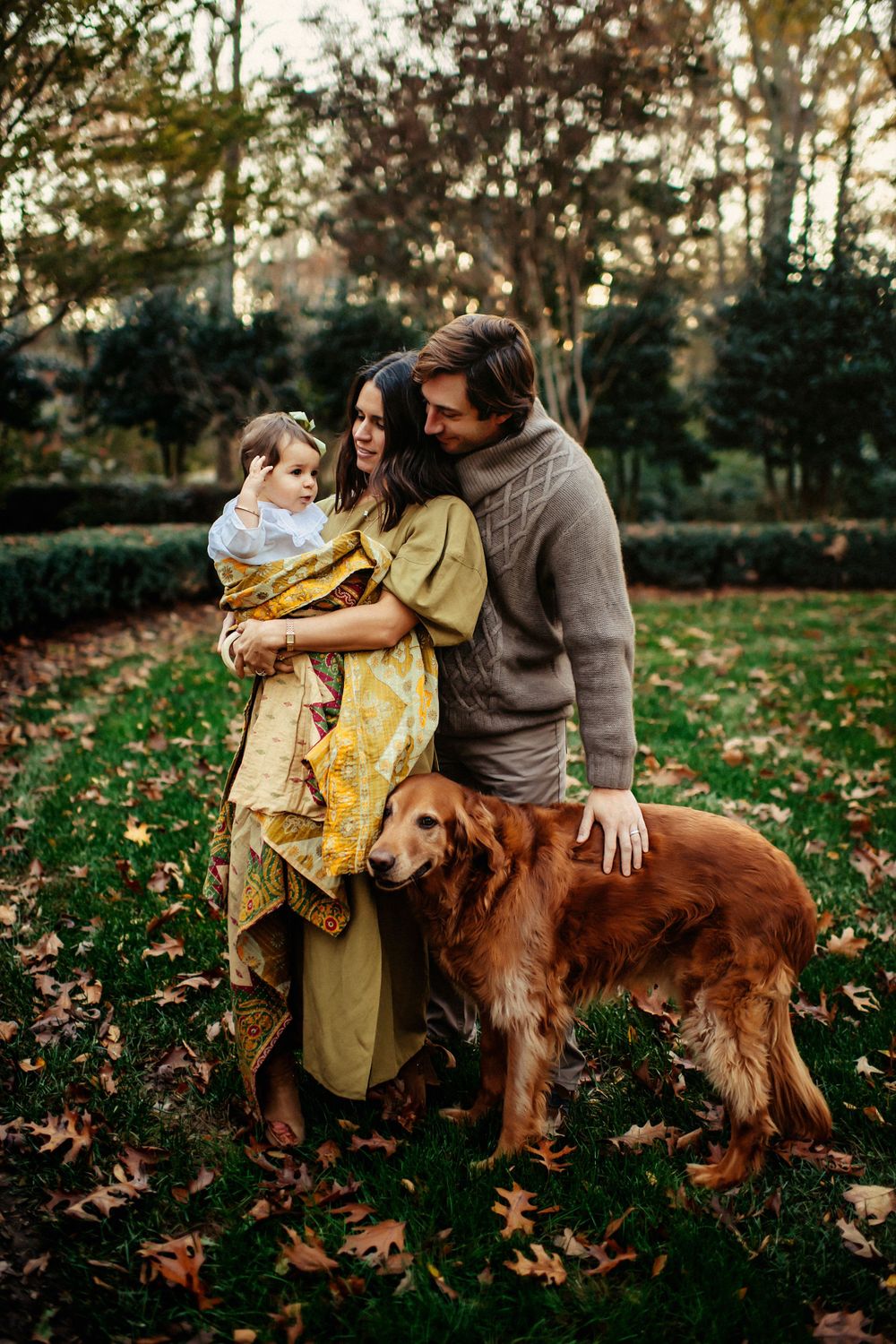 A cozy autumn scene with a family and their golden retriever enjoying fallen leaves in a garden at sunset.