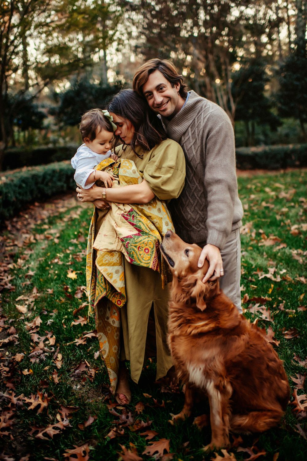 A loving family embraces together on an autumn day with their golden retriever in a wooded setting.