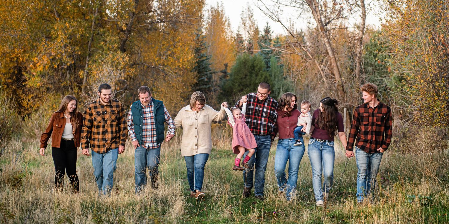 A group dressed in casual light-colored clothing poses together on rocky riverbank with forest in background.