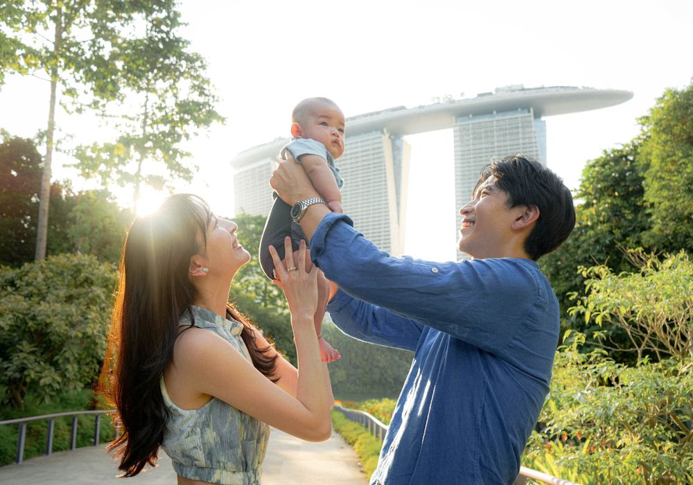 A couple lifting their baby against the backdrop of Marina Bay Sands in Singapore's Gardens by the Bay.