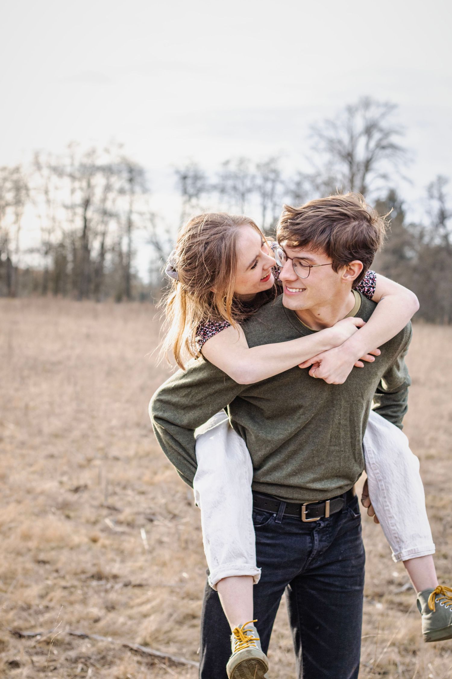 a woman is carried on the back of a man, they smile at each other as they walk through a golden field