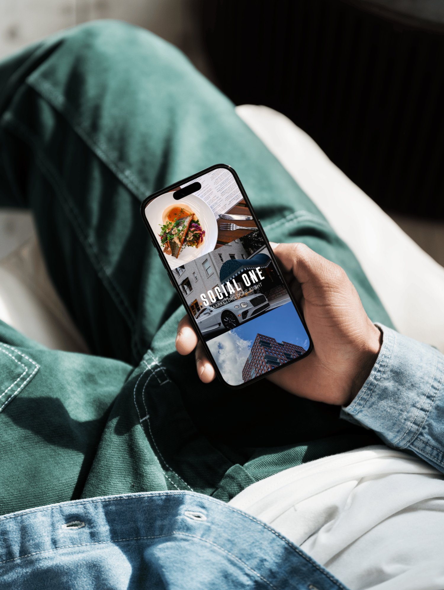 Person holding phone displaying travel and food photography while sitting in casual denim and green clothing.