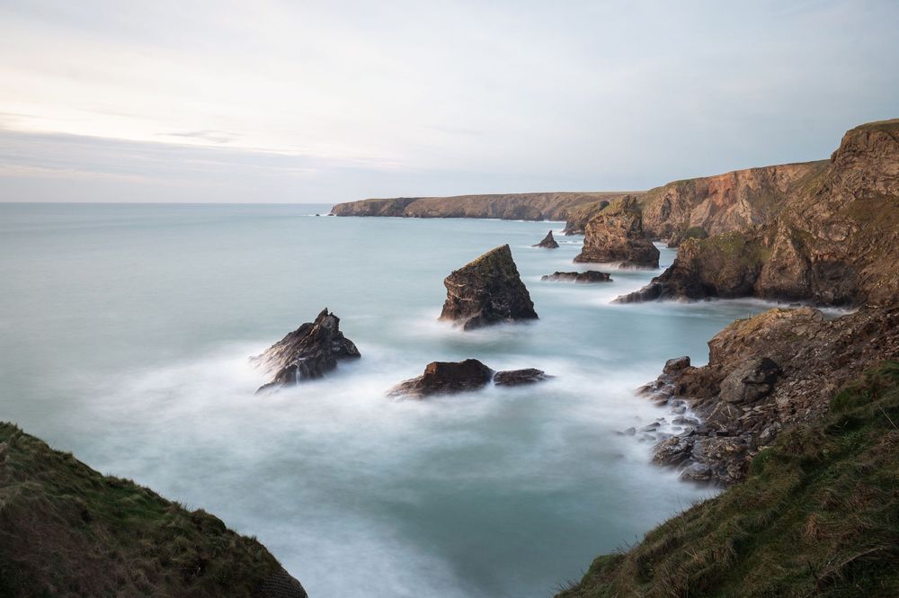 Misty seascape of rugged coastal cliffs and rock formations along the Cornwall coast with smooth flowing waters.