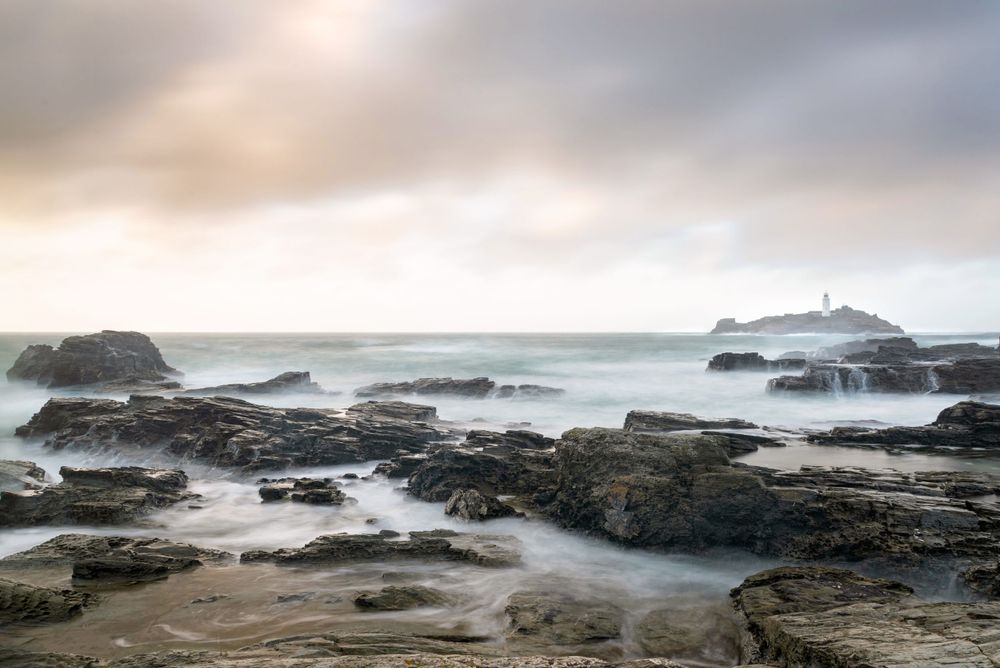 Long exposure seascape with misty waves crashing over rocky coast and lighthouse in foggy distance at Yaquina Head, Oregon.