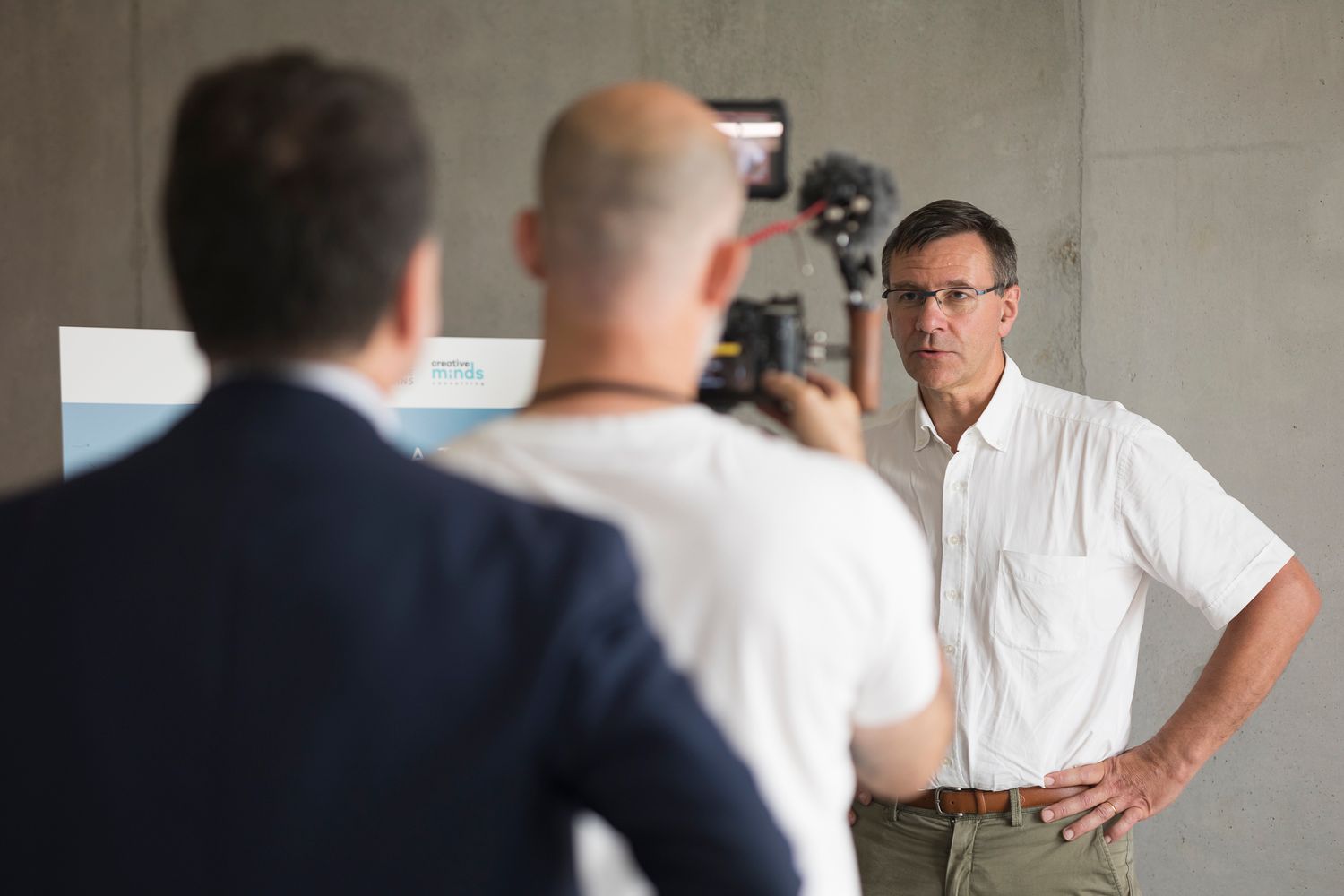 Behind-the-scenes filming setup with camera crew and subject in white shirt.