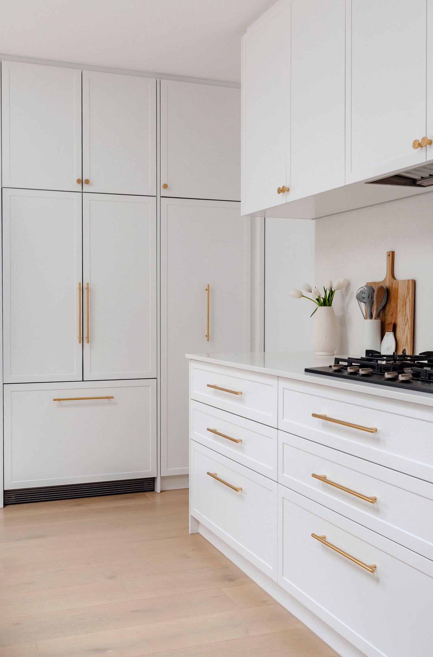 Contemporary white kitchen featuring tall cabinets with brass hardware and gas cooktop.