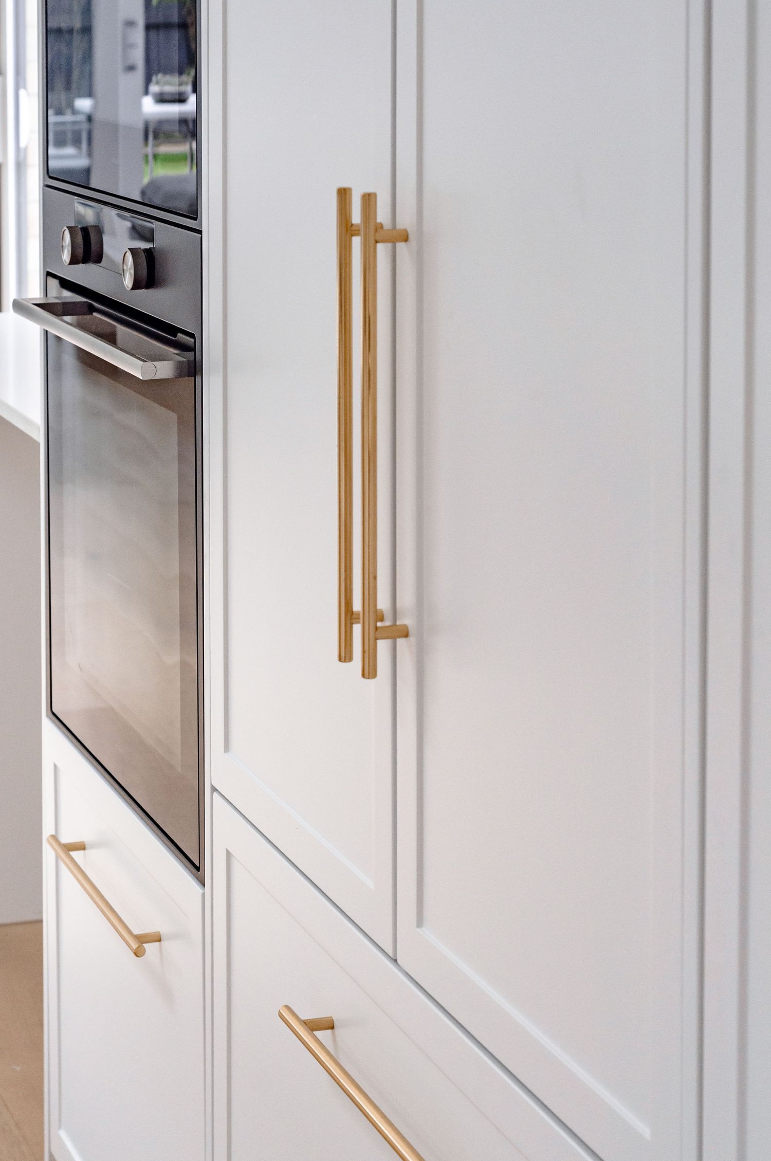 Modern kitchen cabinet with sleek white panels and brushed gold handles and hardware.