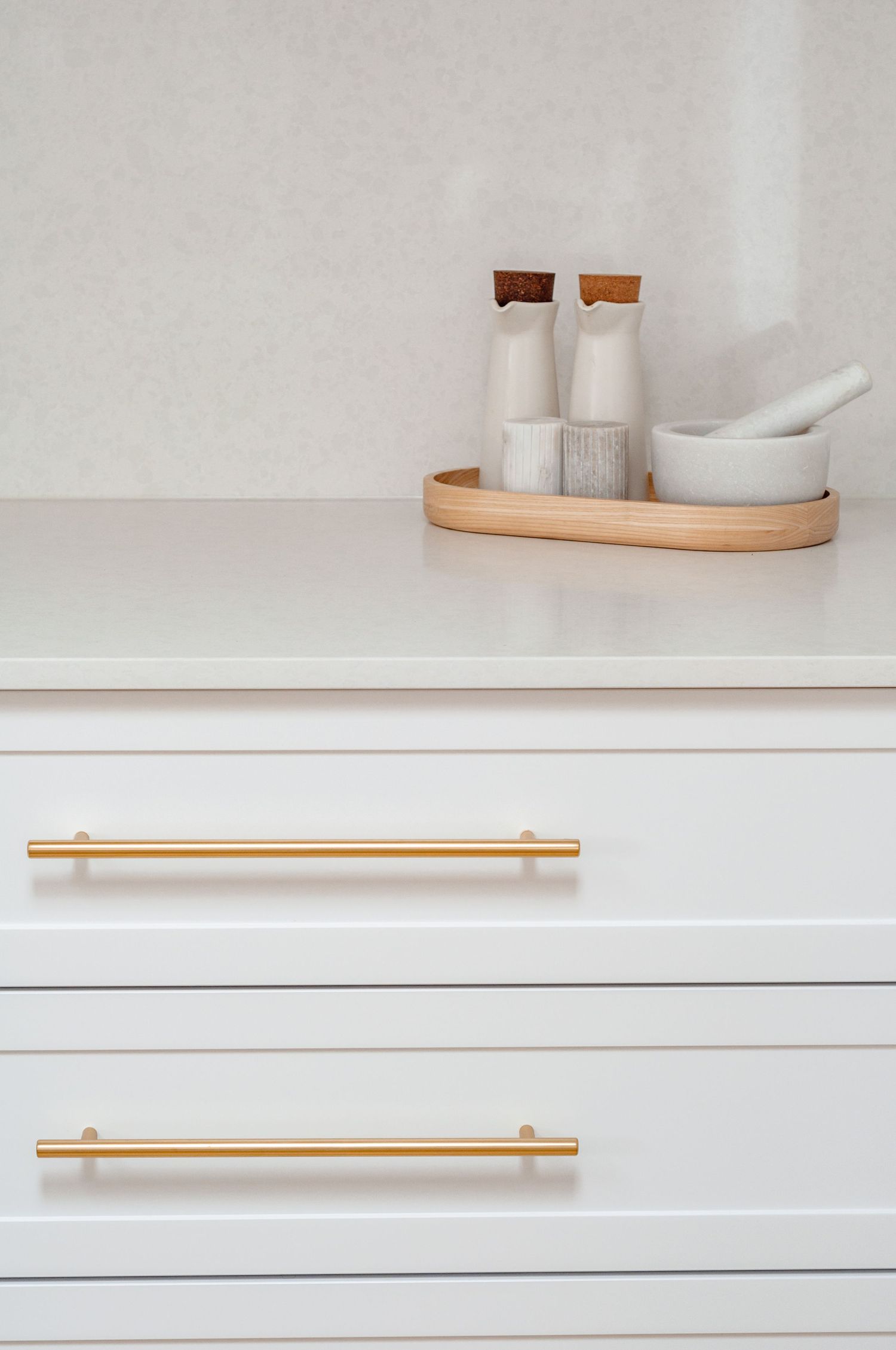 Minimalist white dresser with gold handles featuring a wooden tray holding ceramic dispensers and mortar bowl on top.