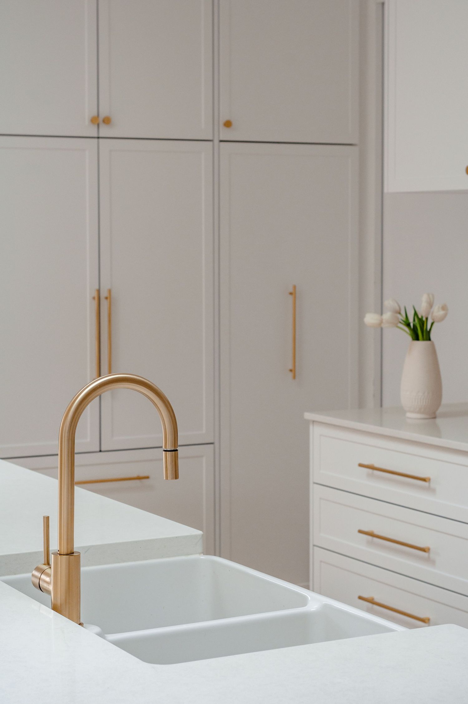 Modern white kitchen featuring a brass faucet, double sink and cabinets with matching brass hardware.