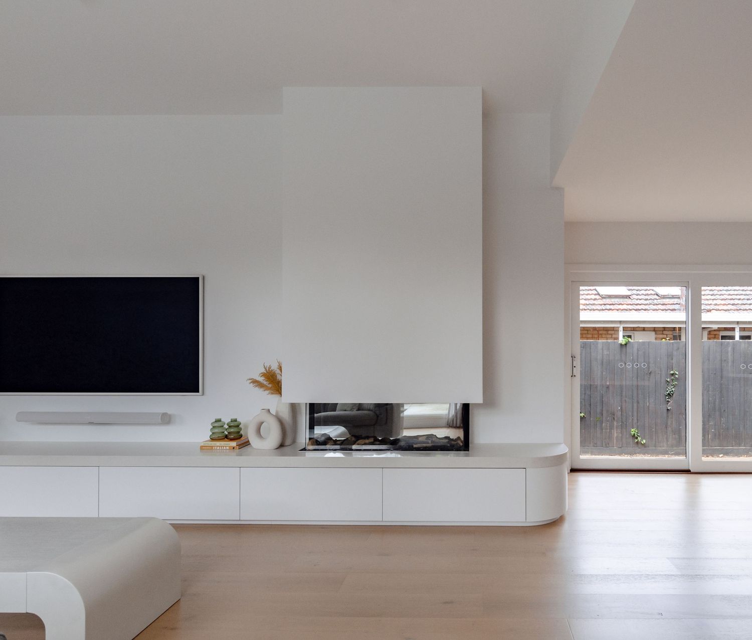 Modern minimalist living room with floating white media unit, hardwood floors, and floor-to-ceiling windows.
