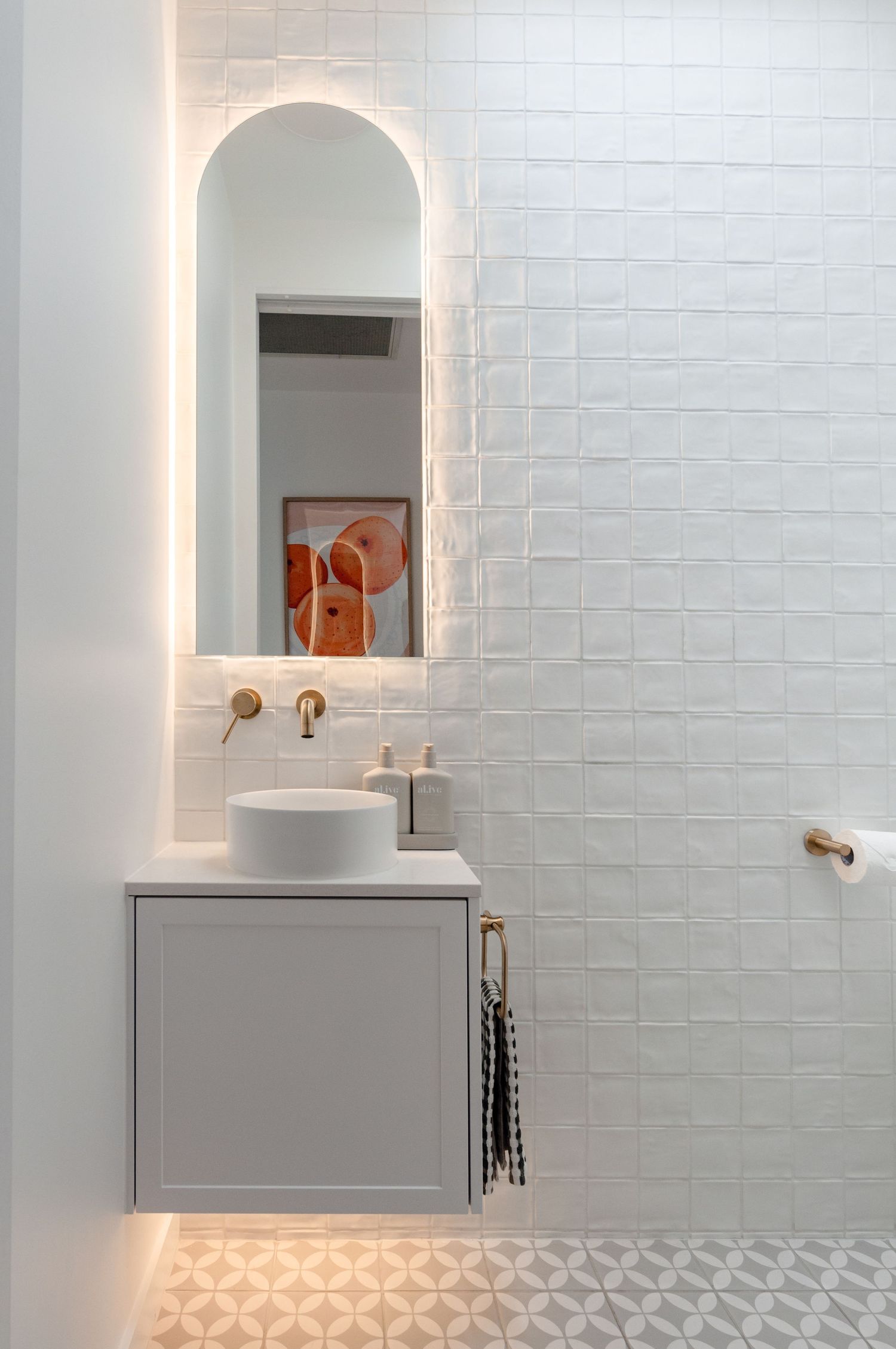 Modern bathroom with arched backlit mirror, white vessel sink, and gray vanity against white tile walls.