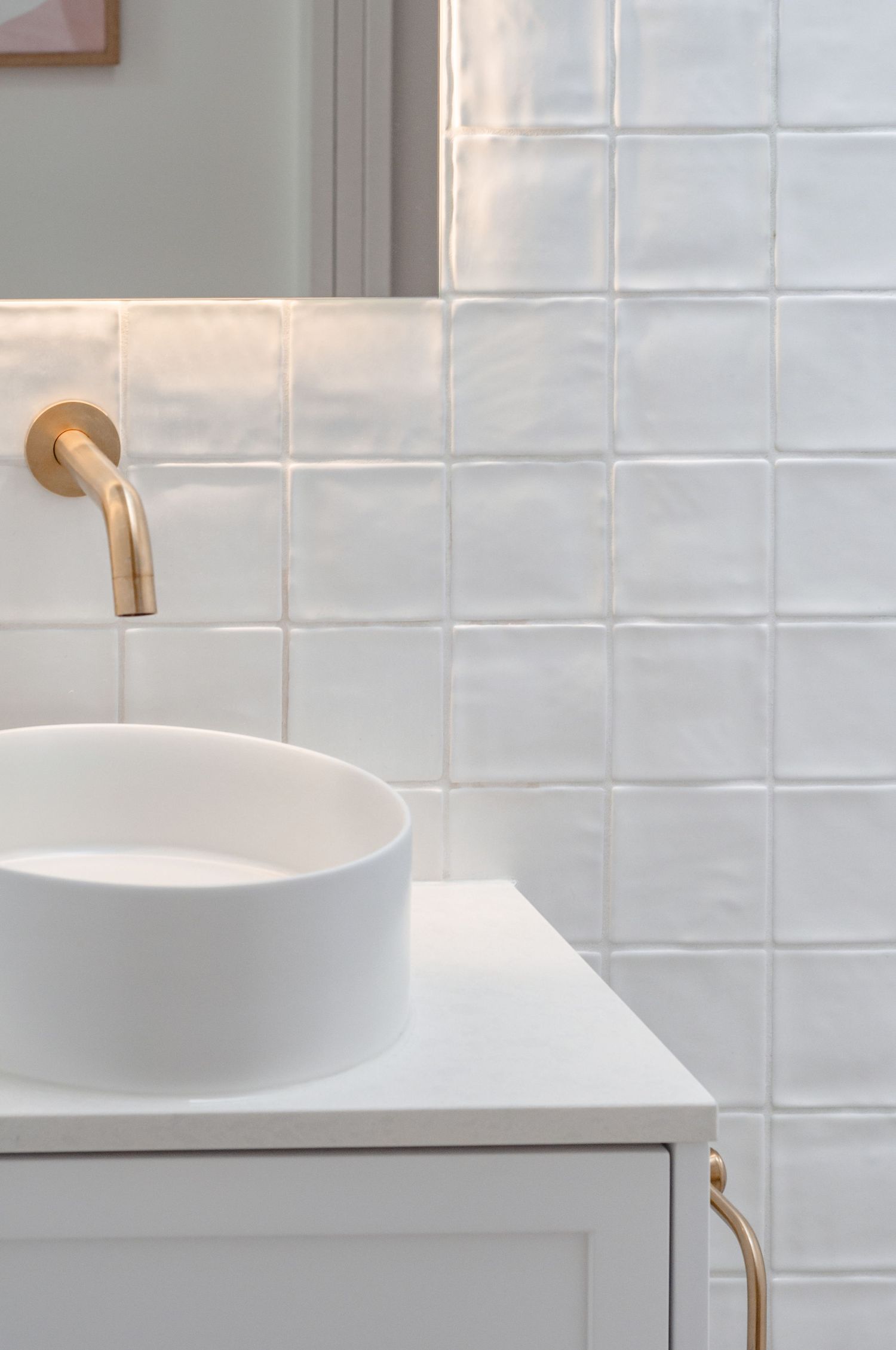 Modern white bathroom vanity with vessel sink and brass wall-mounted faucet against white geometric tile backsplash.