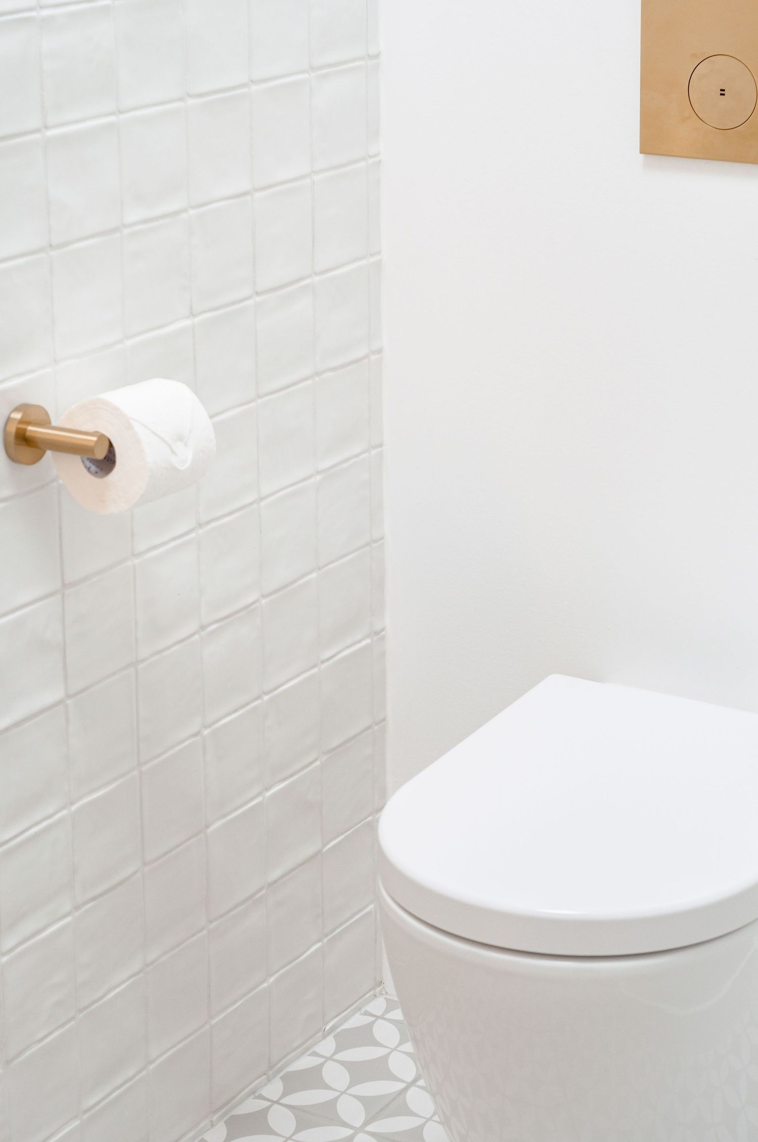 White minimalist bathroom with subway tile walls, wooden toilet paper holder, and geometric patterned floor.