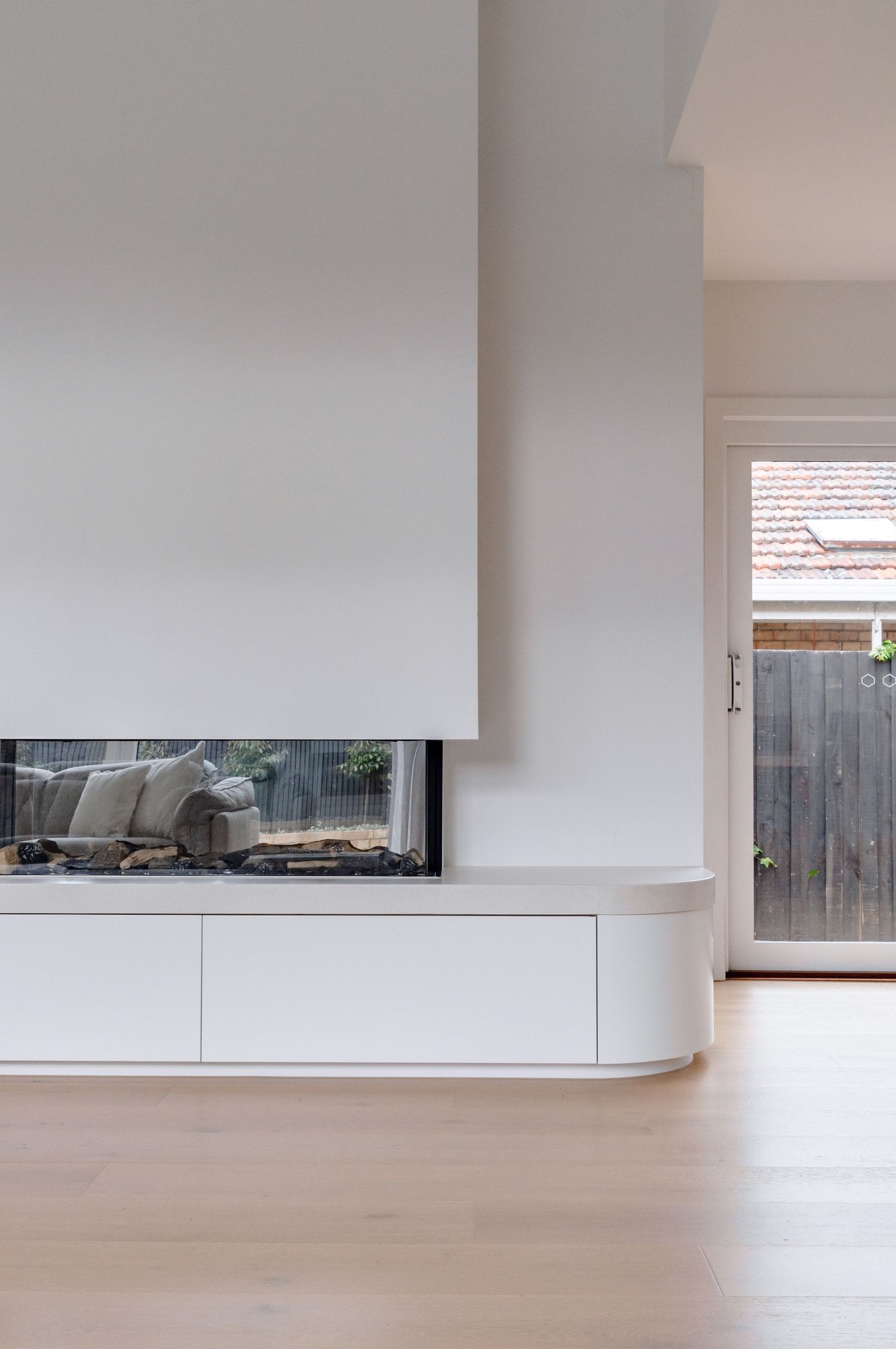 Minimalist white living room with a sleek built-in fireplace and hardwood flooring.