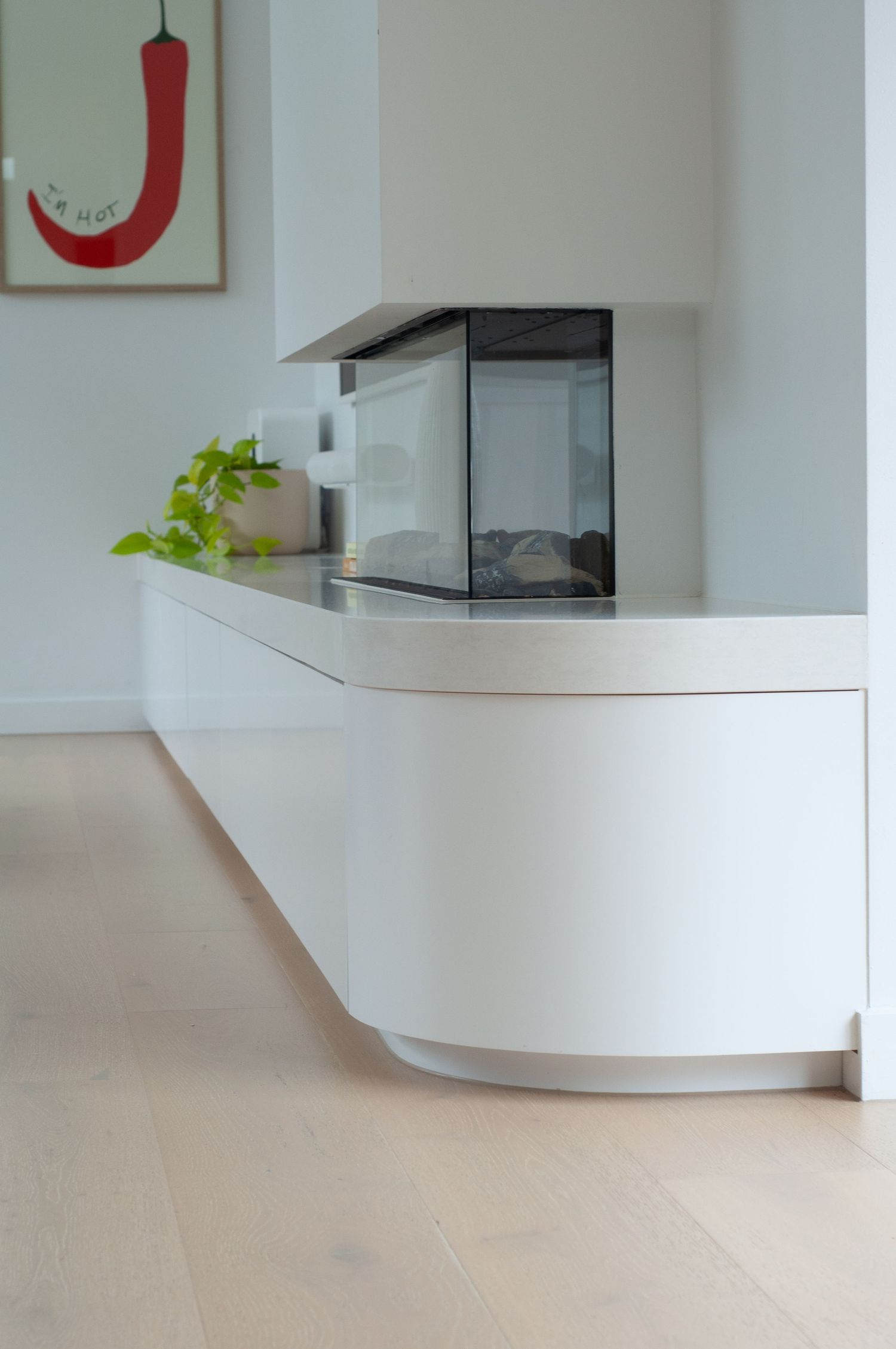 Modern white cabinet with floating design features a small terrarium display and green plant on sleek countertop surface.