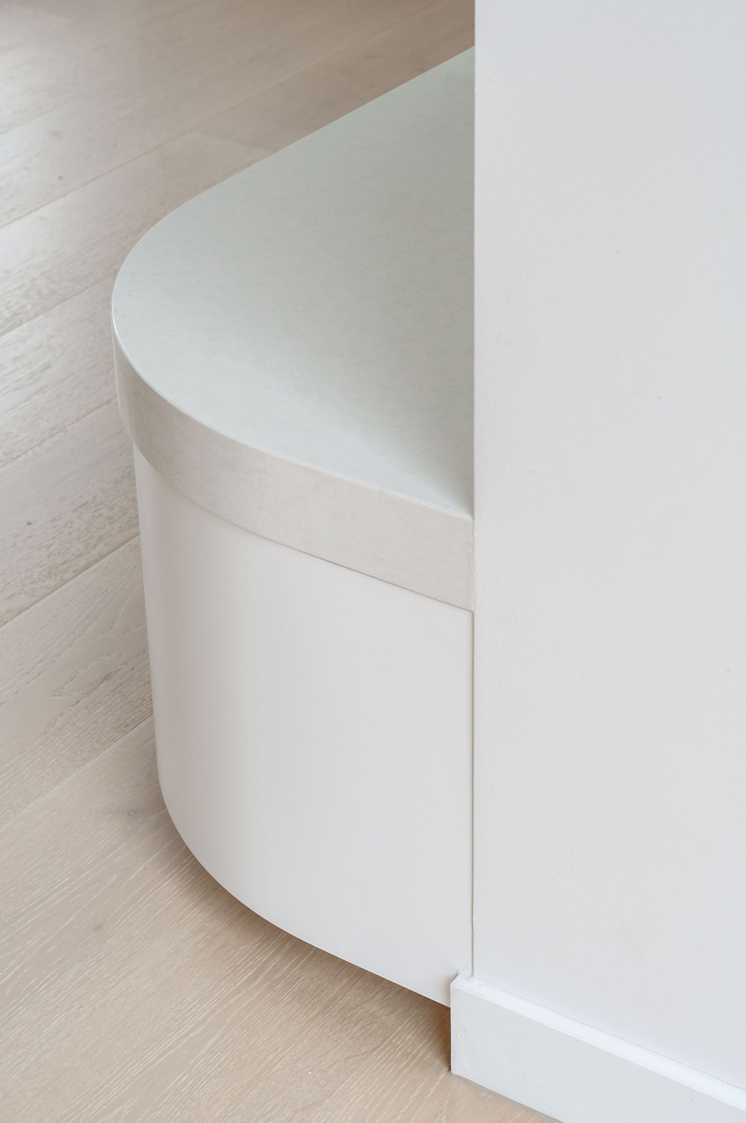 Minimalist curved white architectural detail showing a rounded corner baseboard against light wood flooring.