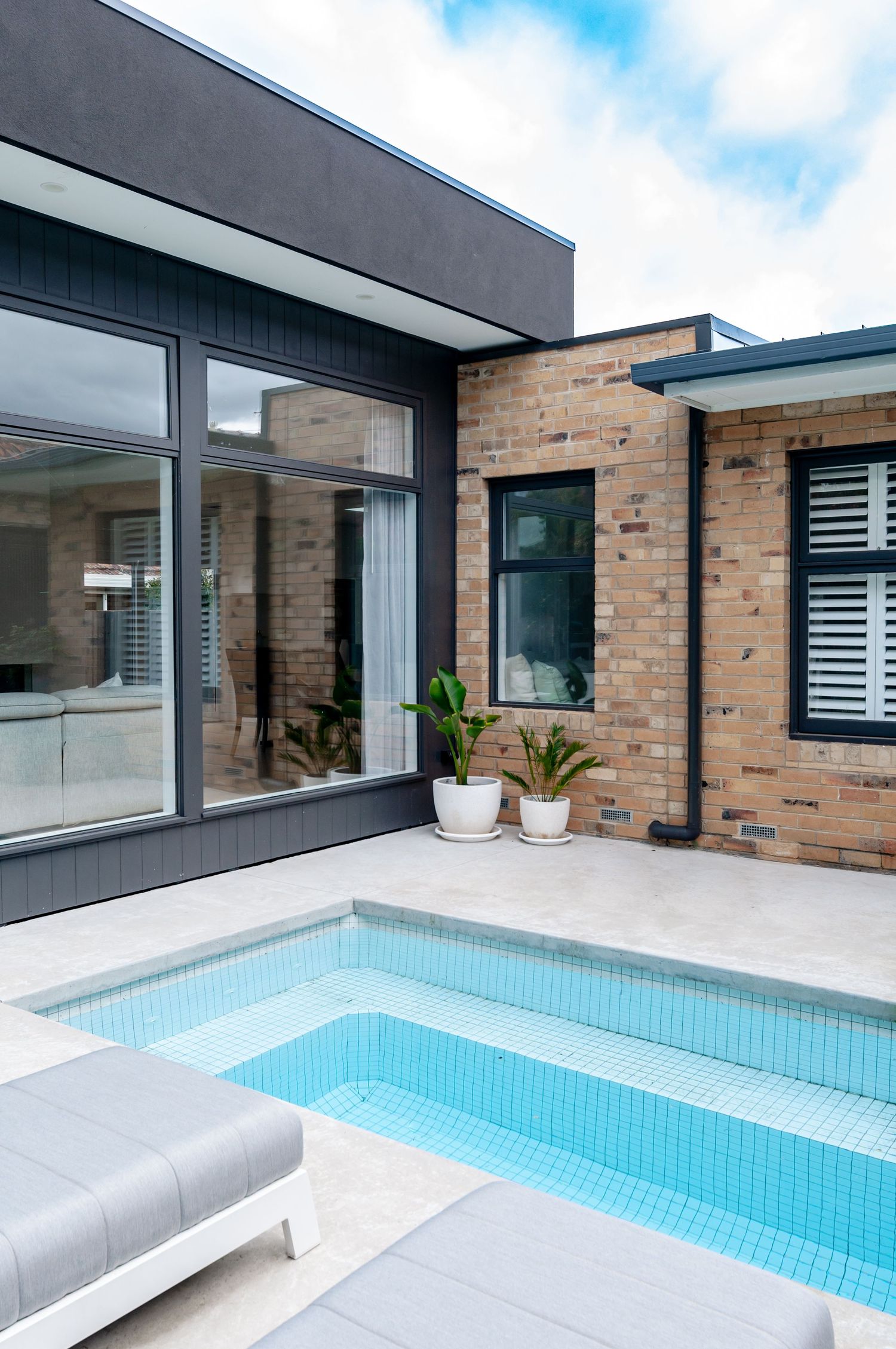 Contemporary home exterior with pool, featuring glass windows, brick walls, and gray accents on a sunny day.