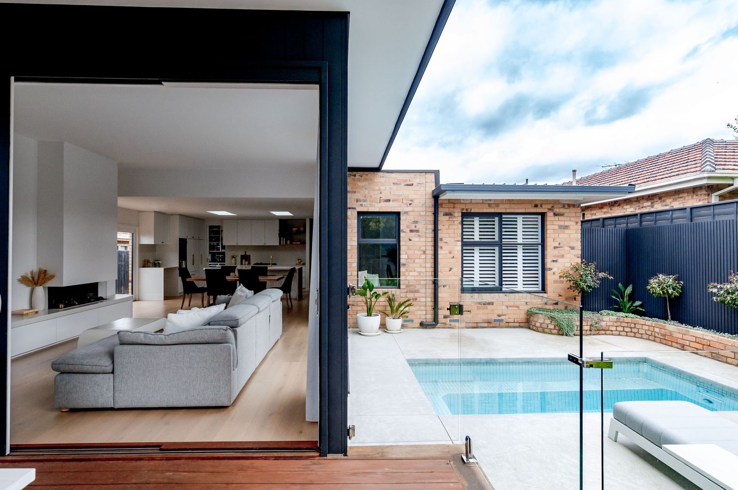 Modern indoor-outdoor living space with gray sofa overlooking a swimming pool through large sliding doors.