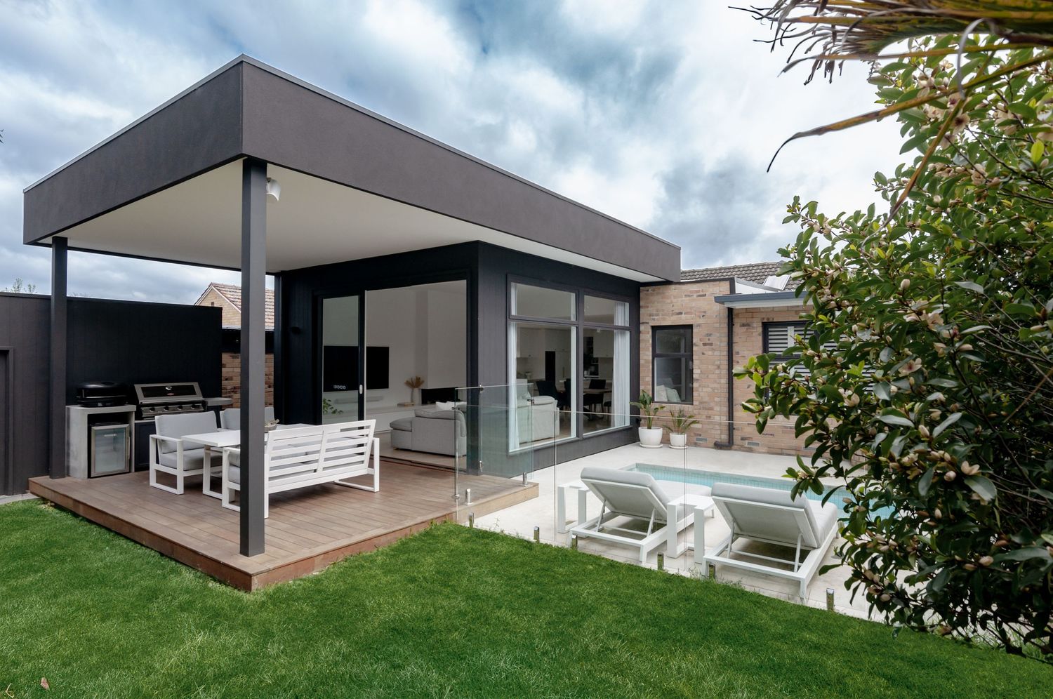 Modern outdoor covered patio with plush seating area and lawn overlooking sunken lounge space in contemporary backyard design.