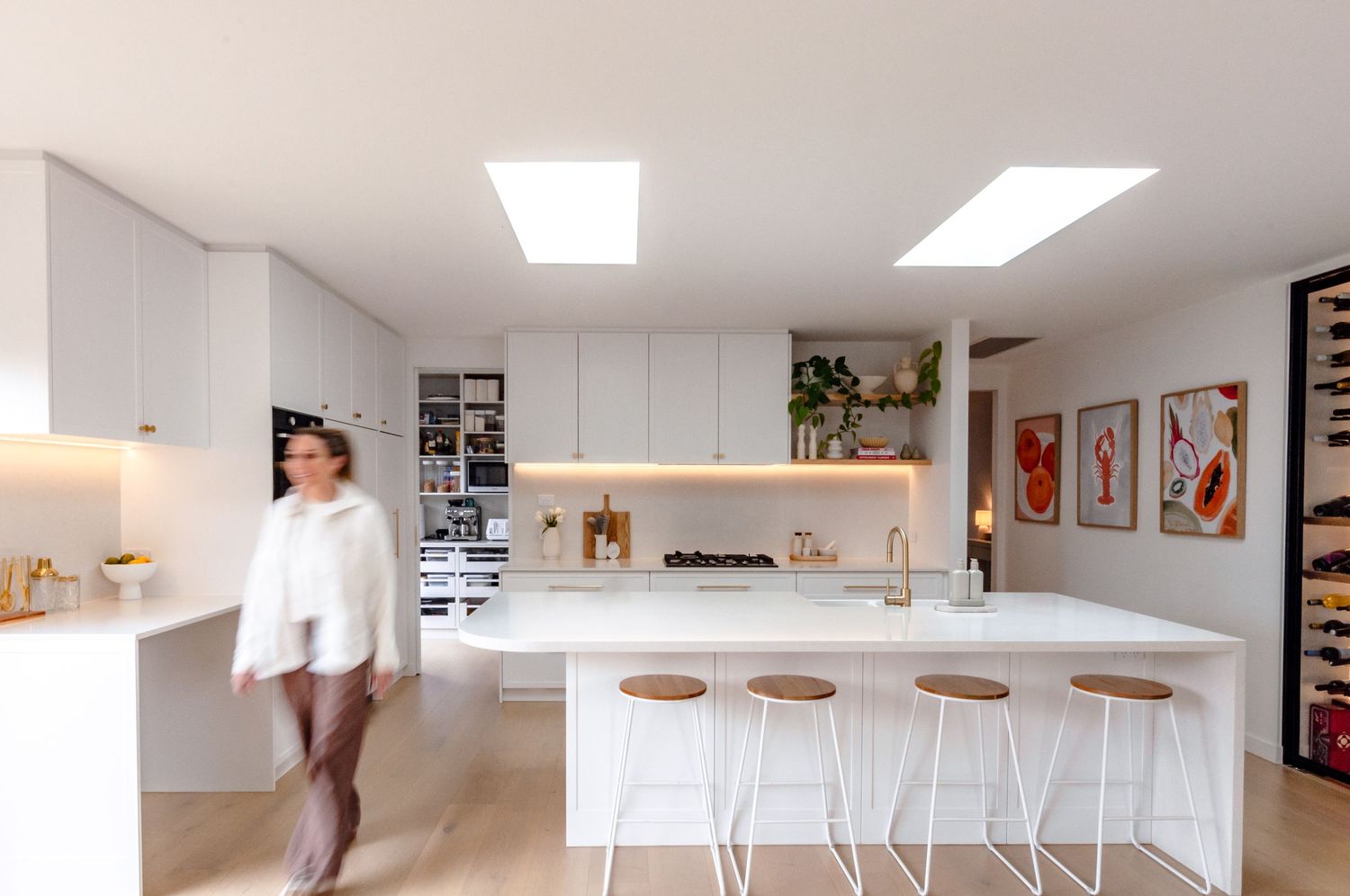 Modern white kitchen with minimalist design featuring bar seating, floating shelves and colorful wall art.