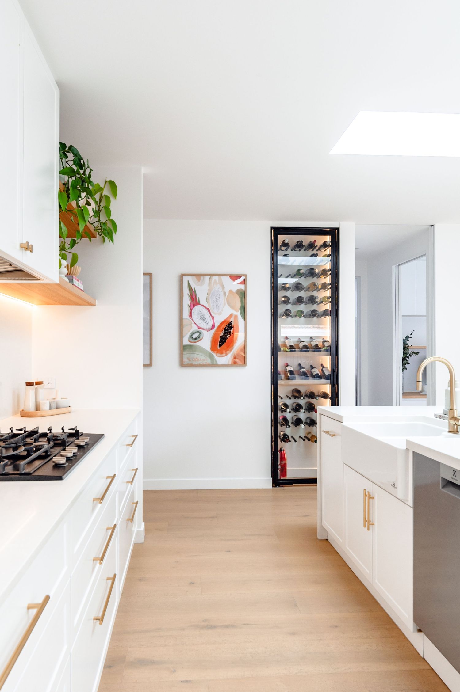 Modern white kitchen with built-in wine refrigerator, gas range, and decorative artwork on wall.