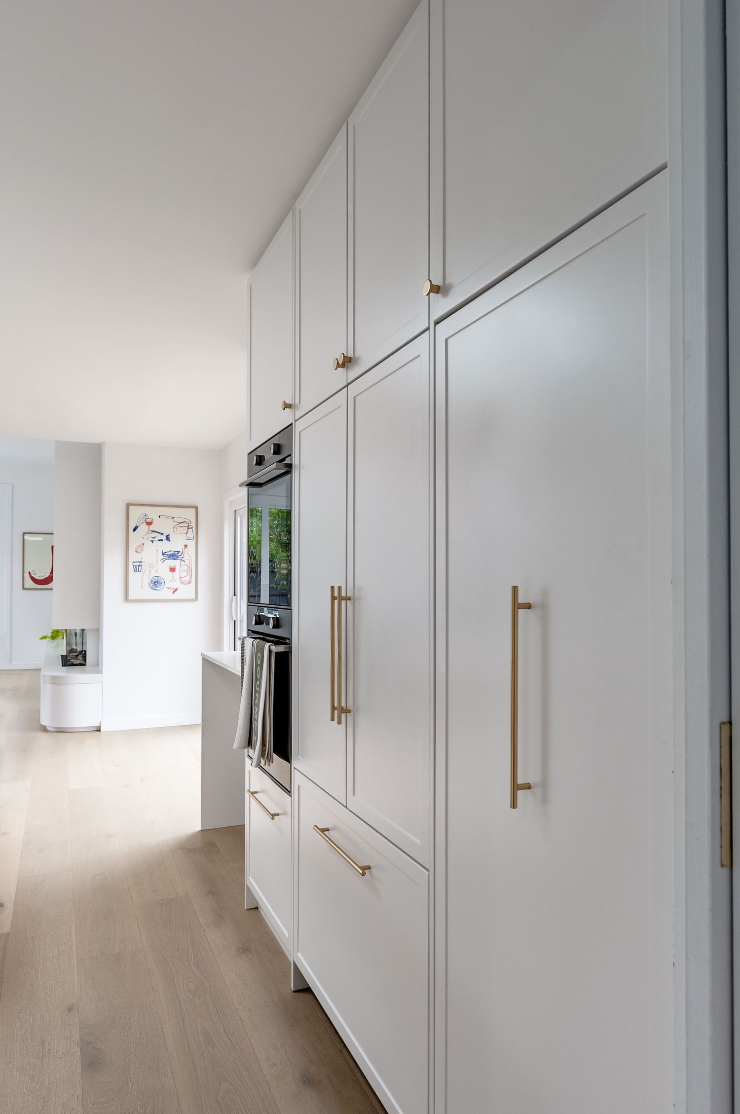 White floor-to-ceiling kitchen cabinets with brass handles and built-in appliances.