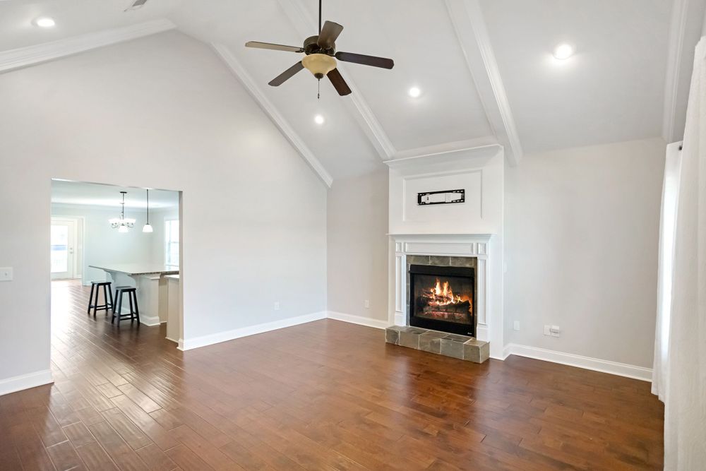 Open concept living space with vaulted ceiling, hardwood floors, and elegant fireplace in white interior.