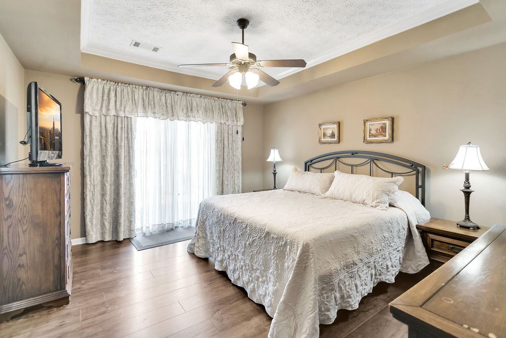 Traditional bedroom with lace bedding, ceiling fan, and elegant window treatments.