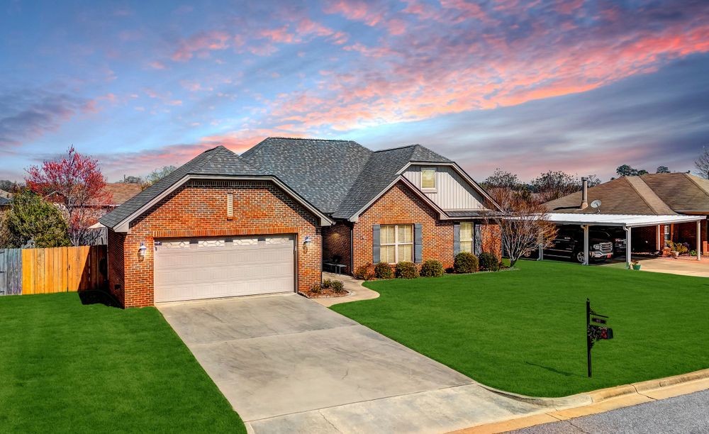 Brick ranch home with attached garage and well-maintained lawn under colorful sunset sky.