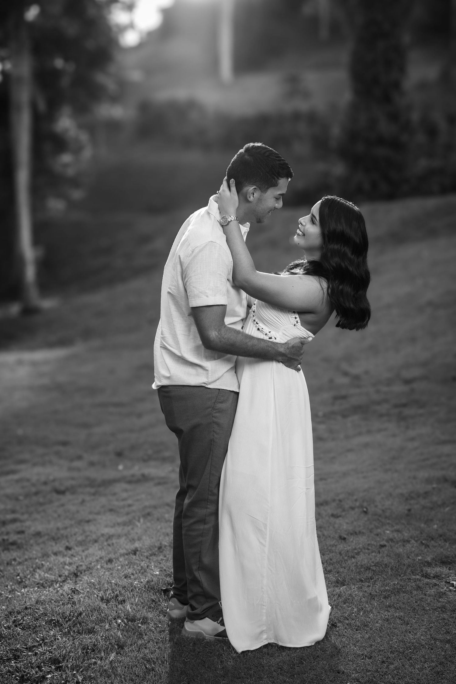 A romantic black and white portrait of a couple embracing outdoors in a dreamy garden setting.
