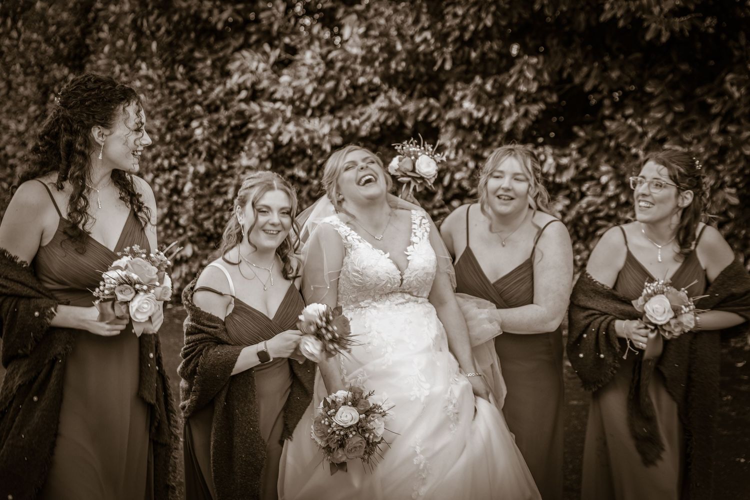 Black and white photo of bridal party sharing joyful laughter outdoors.