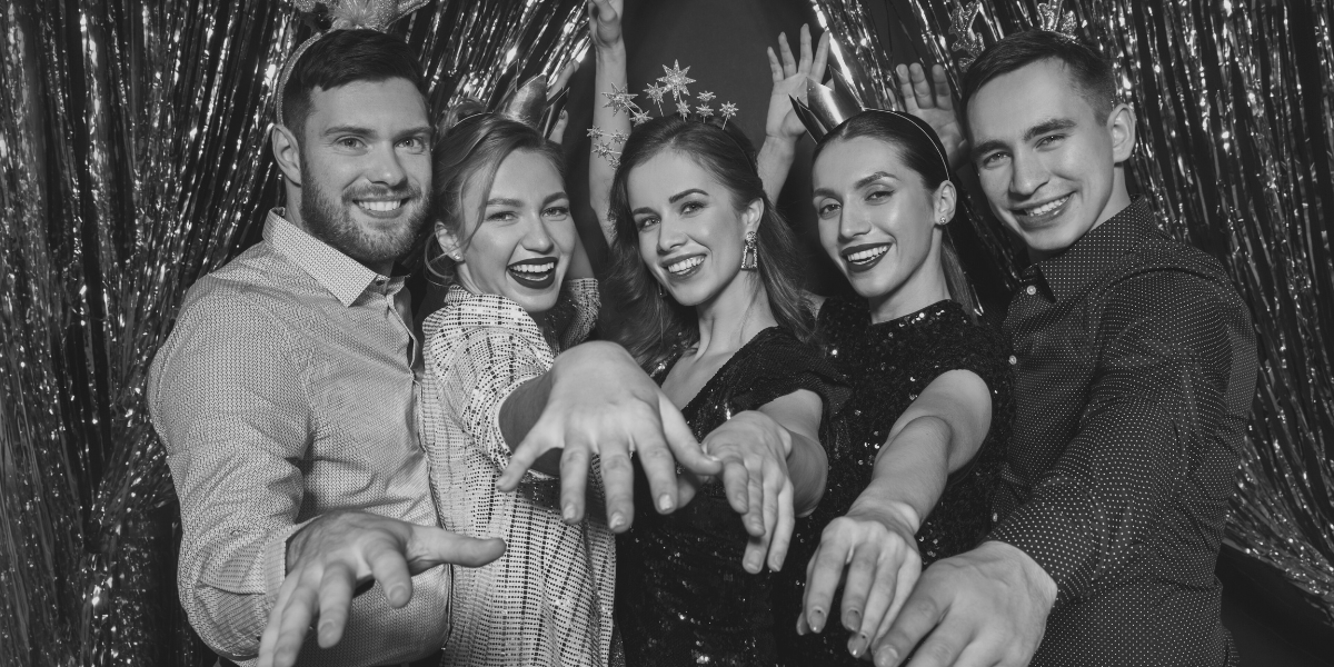 A group of friends show off their rings in a black and white photo with a sparkly backdrop.
