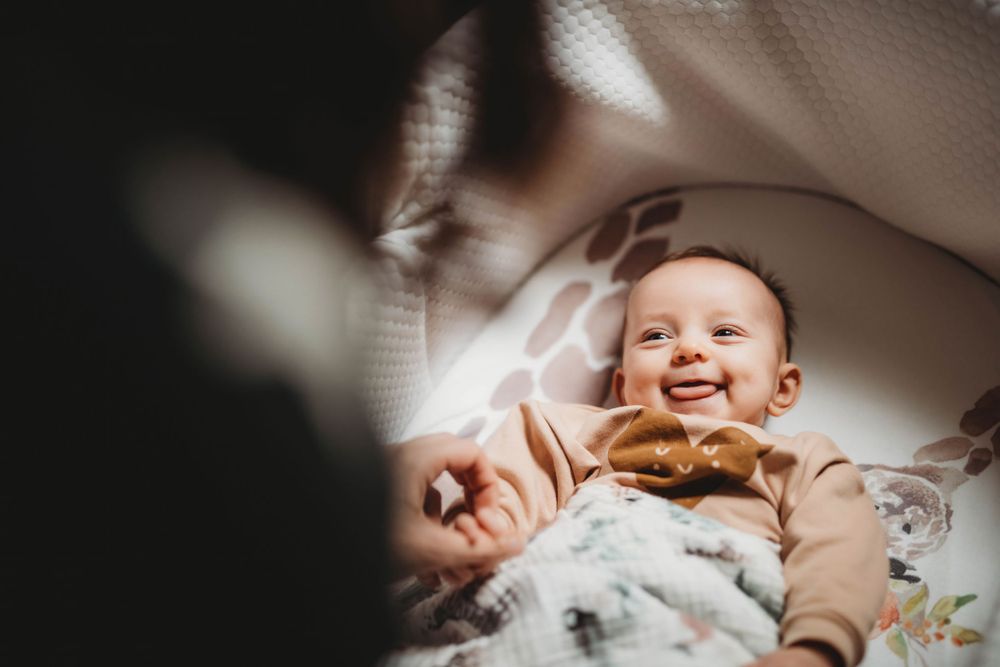 Happy baby in beige outfit smiles brightly while lying down in soft lighting.