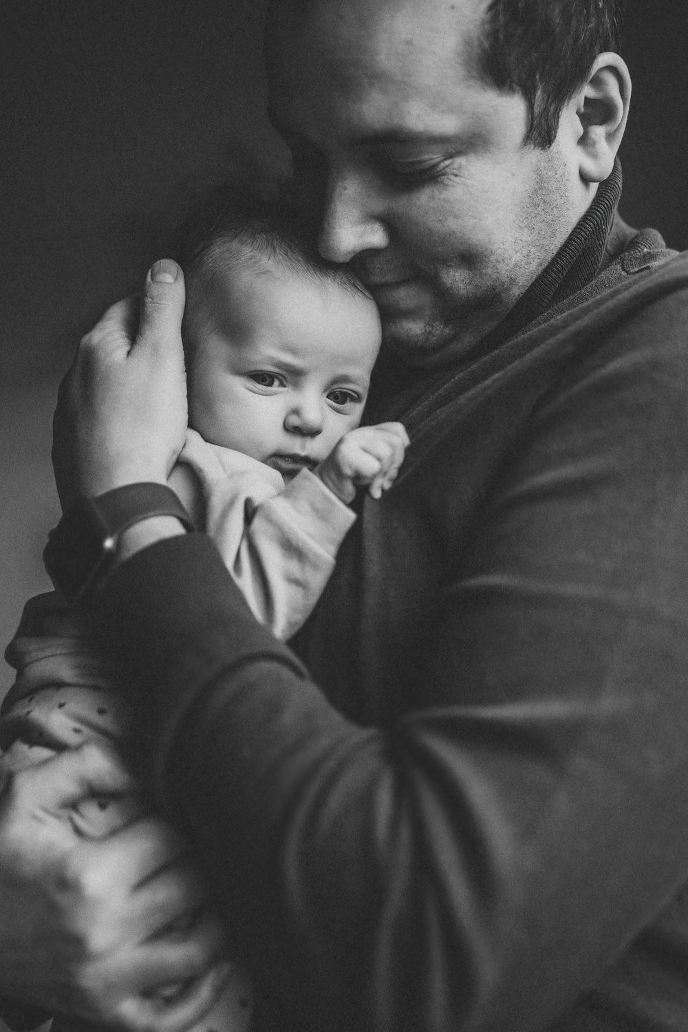 Black and white portrait of tender moment between parent and infant in casual attire.
